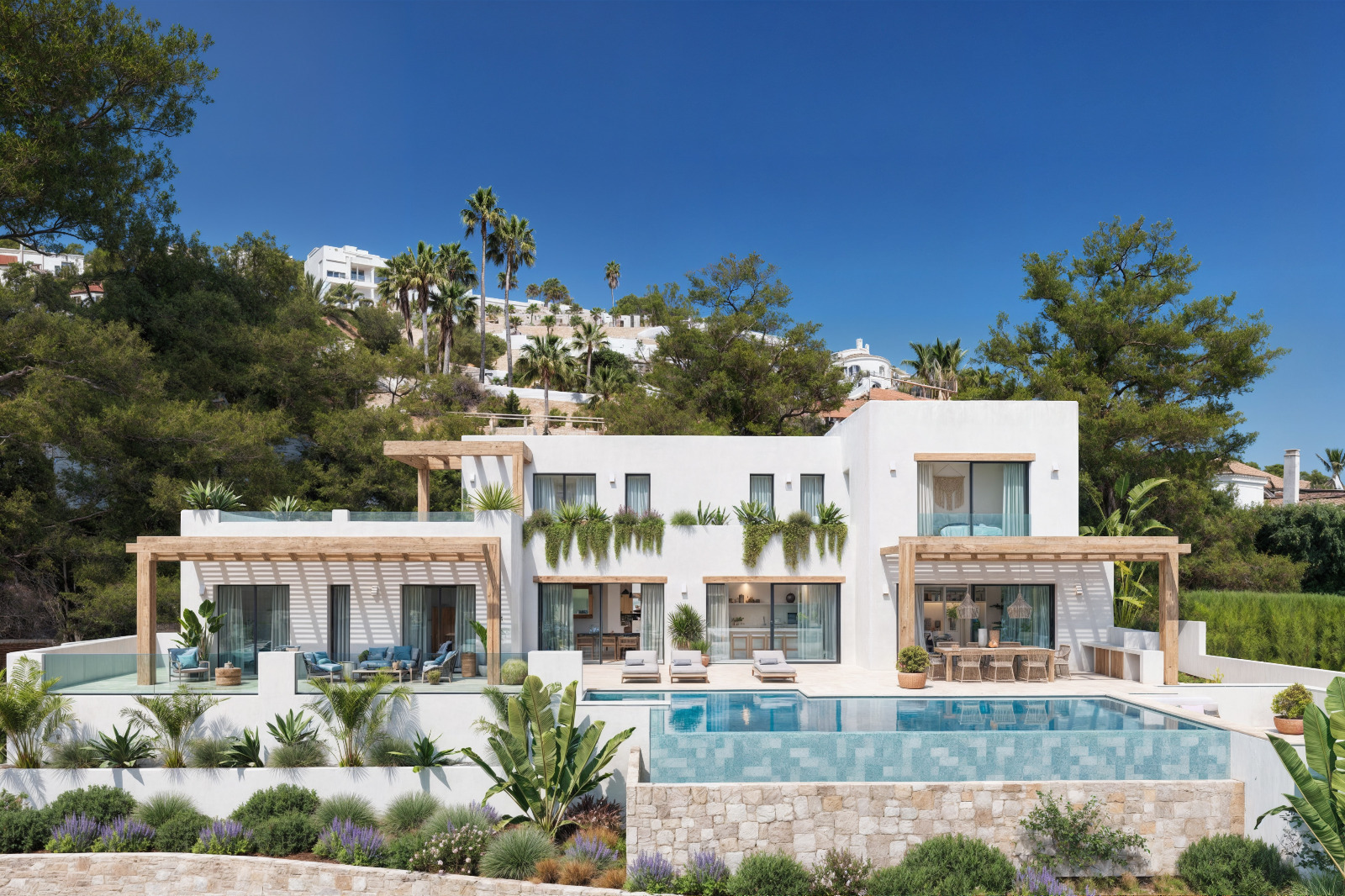 Exterior view of the villa featuring white facades, wooden pergolas, an infinity pool, and a landscaped Mediterranean garden with natural stone walls.