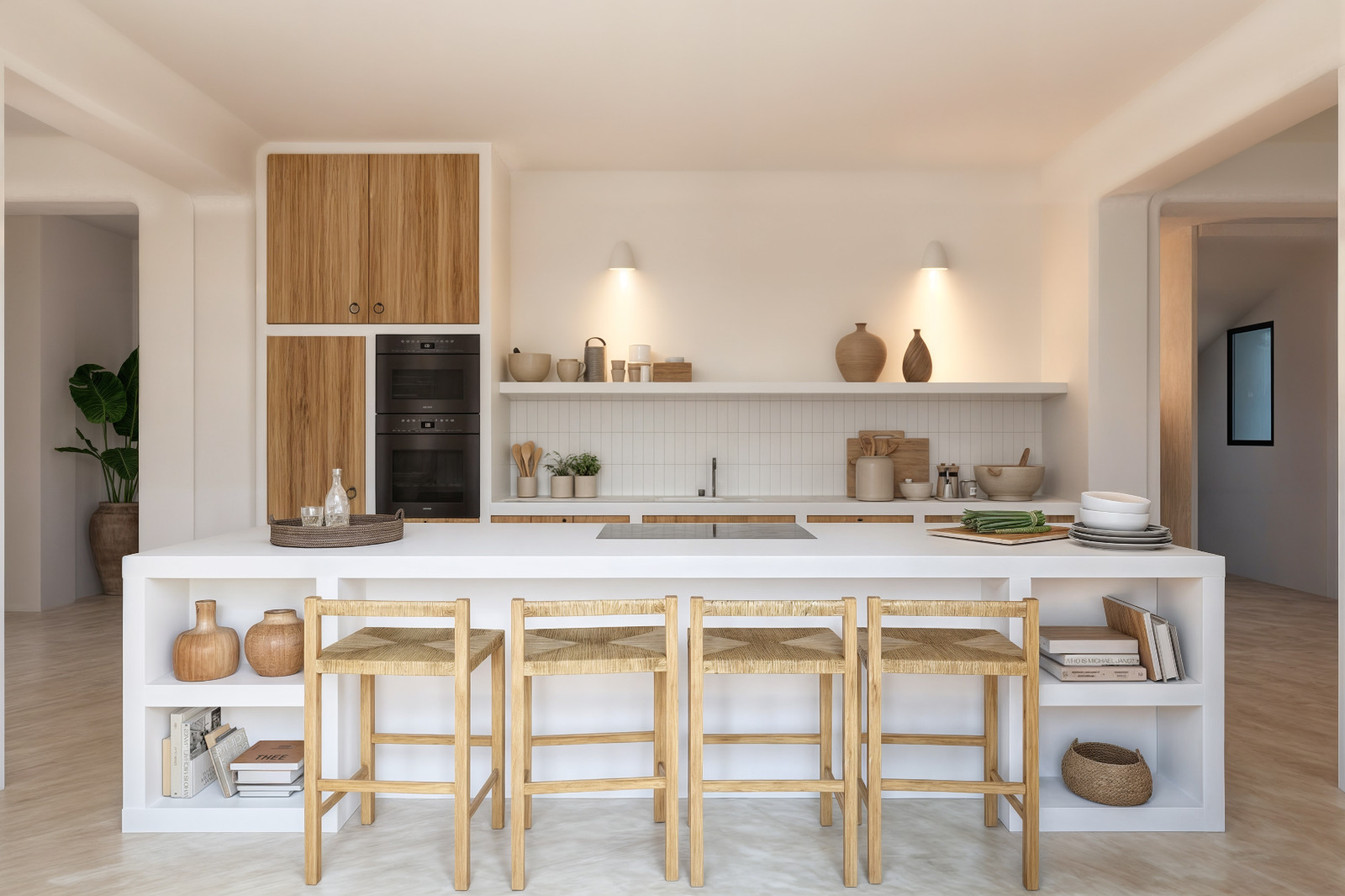 Ibicencan-style kitchen featuring a white island with woven bar stools, integrated black ovens, and open shelving accented by warm wall sconces.