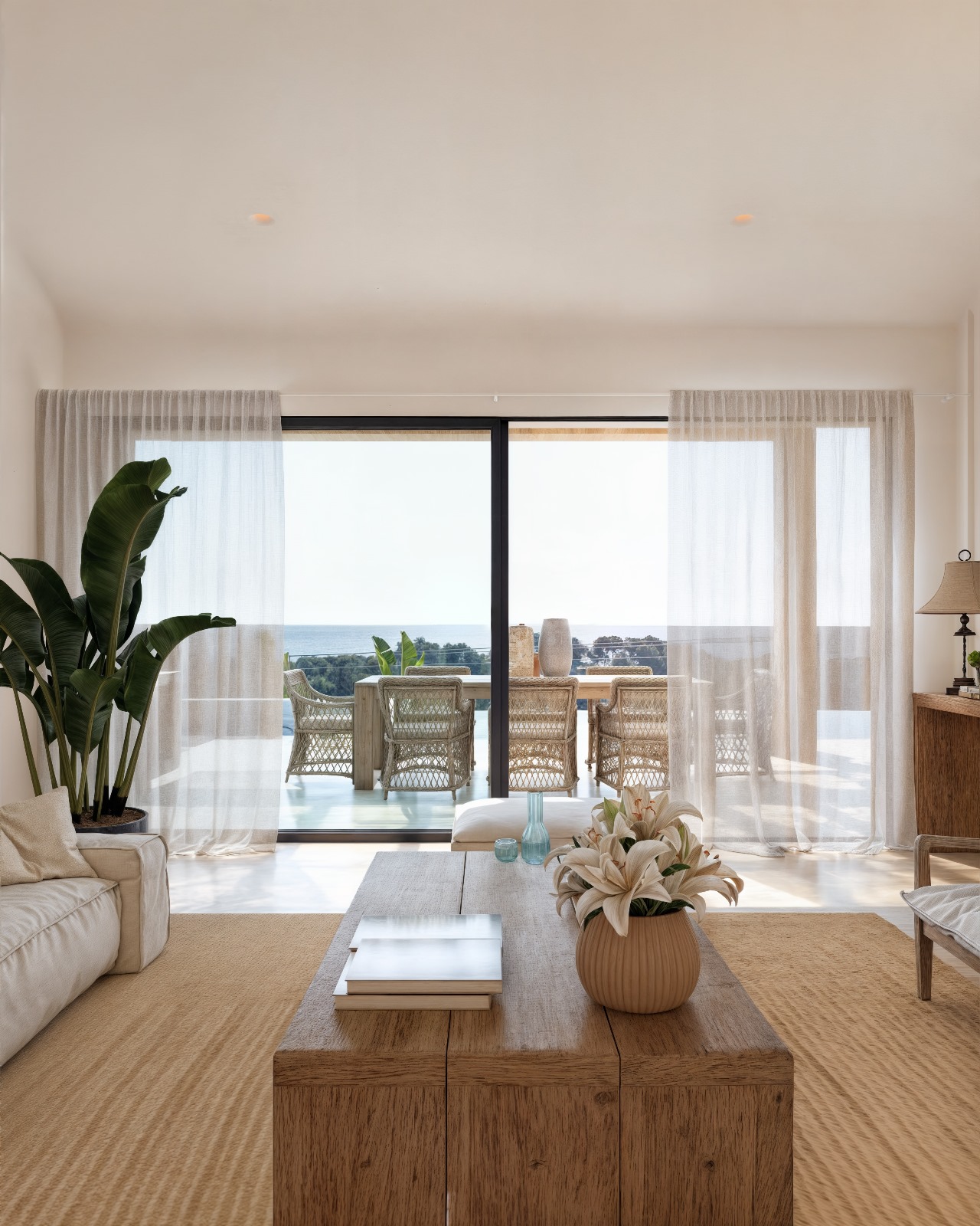 Ibizan-style living area featuring a natural wood coffee table and large sliding doors opening onto a terrace with sea views and wicker seating.