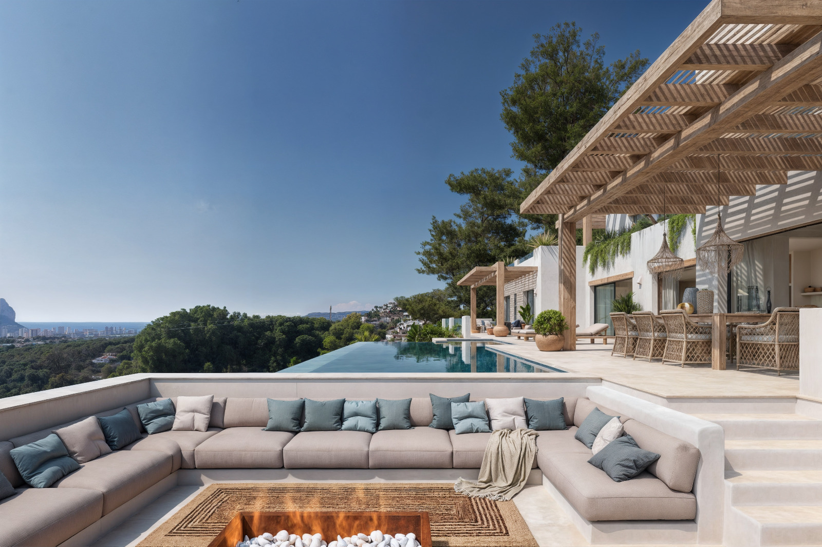 Sunken outdoor lounge with a central fire pit, wooden pergola shading the dining area, and an infinity pool overlooking the Mediterranean Sea and Peñón de Ifach.