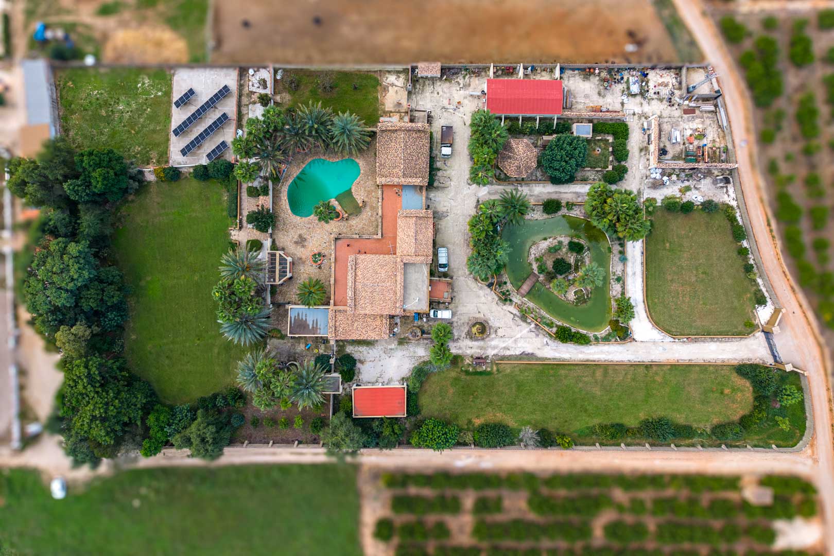 Aerial top-down view of the estate featuring the main residence, swimming pool, Japanese pond, expansive lawns, and the solar panel array on the 10,000 m2 plot.