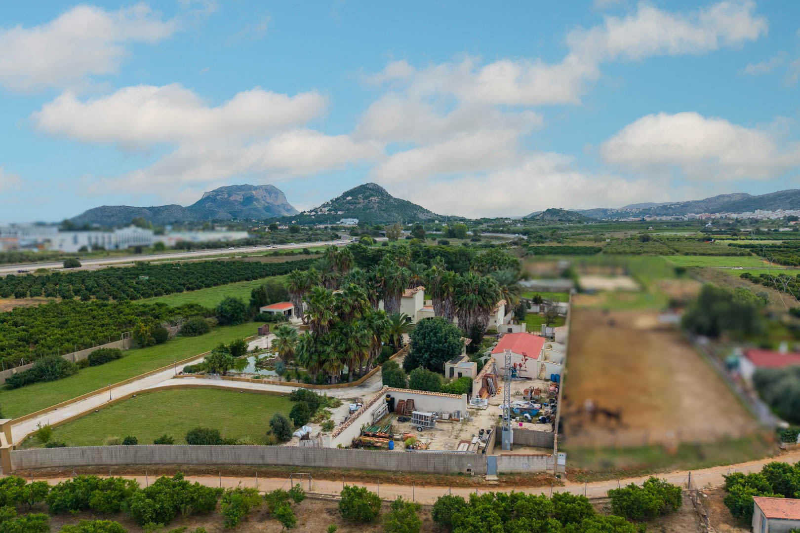 Aerial view of the 10,000 m2 estate in Ondara, featuring lush palm gardens, a central pond, and expansive views of the surrounding valley and mountains.