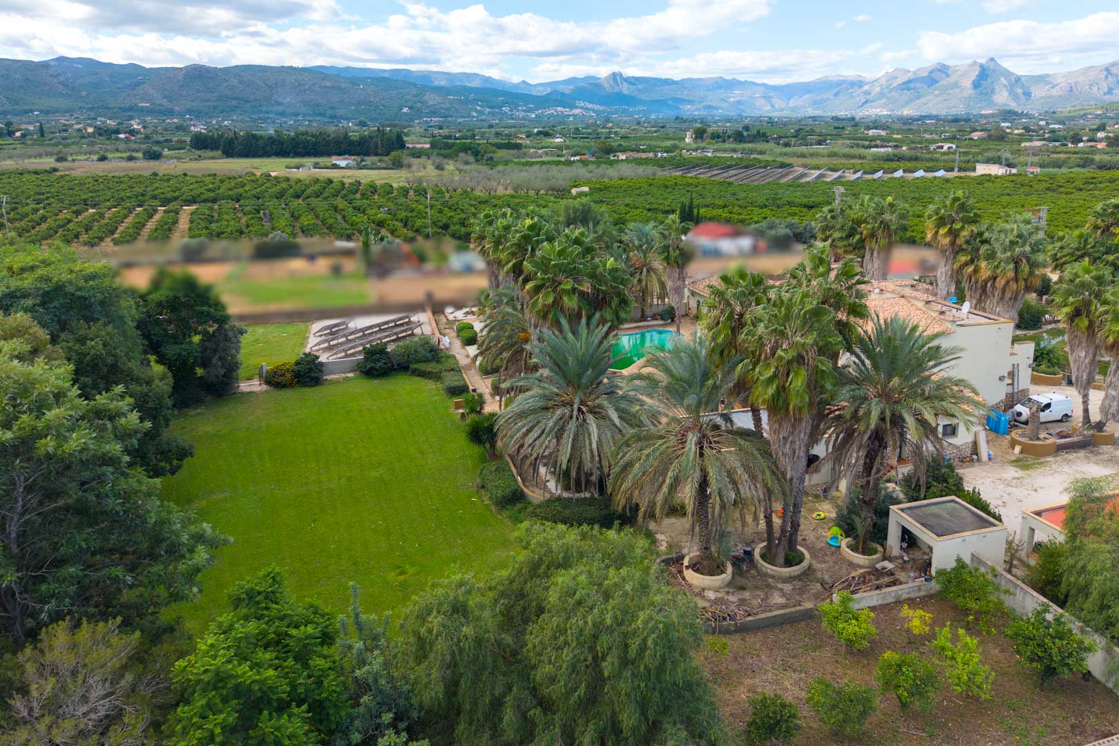 Aerial view of the expansive estate featuring palm-lined gardens, a large lawn, and a swimming pool set against a backdrop of orange groves and mountains.