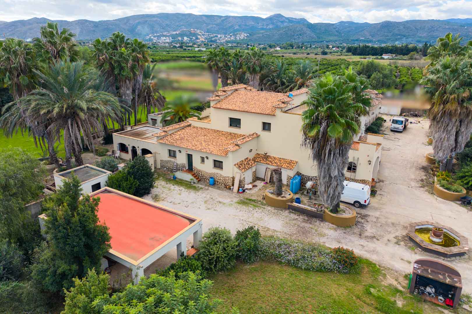 Aerial view of the Mediterranean villa featuring terracotta roofs and cream facades, set within expansive grounds with palms and mountain views.