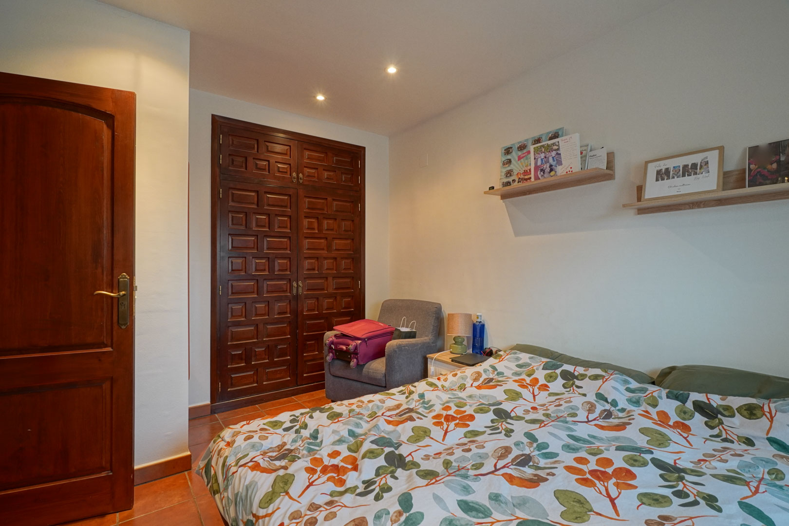 Bedroom featuring a custom dark wood built-in wardrobe with traditional paneling, terracotta tile floors, and recessed ceiling spotlights for a warm ambiance.
