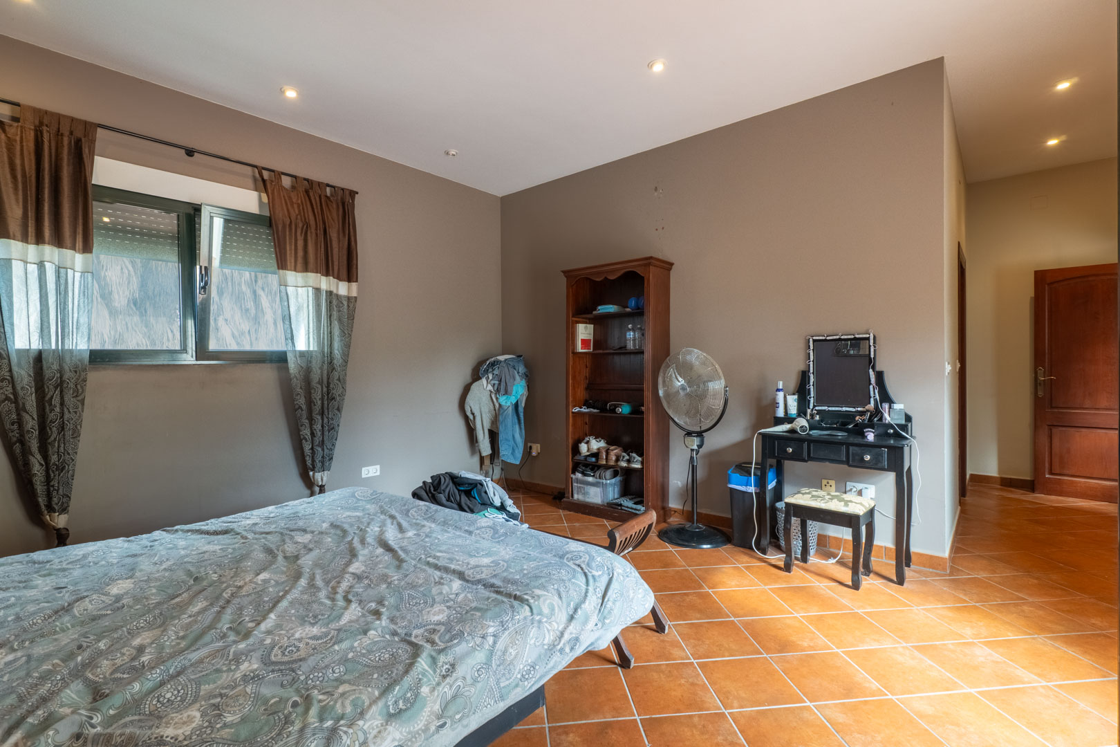 Bedroom featuring diagonal terracotta tile flooring, recessed ceiling spotlights, and neutral-toned walls with a window and integrated blinds.