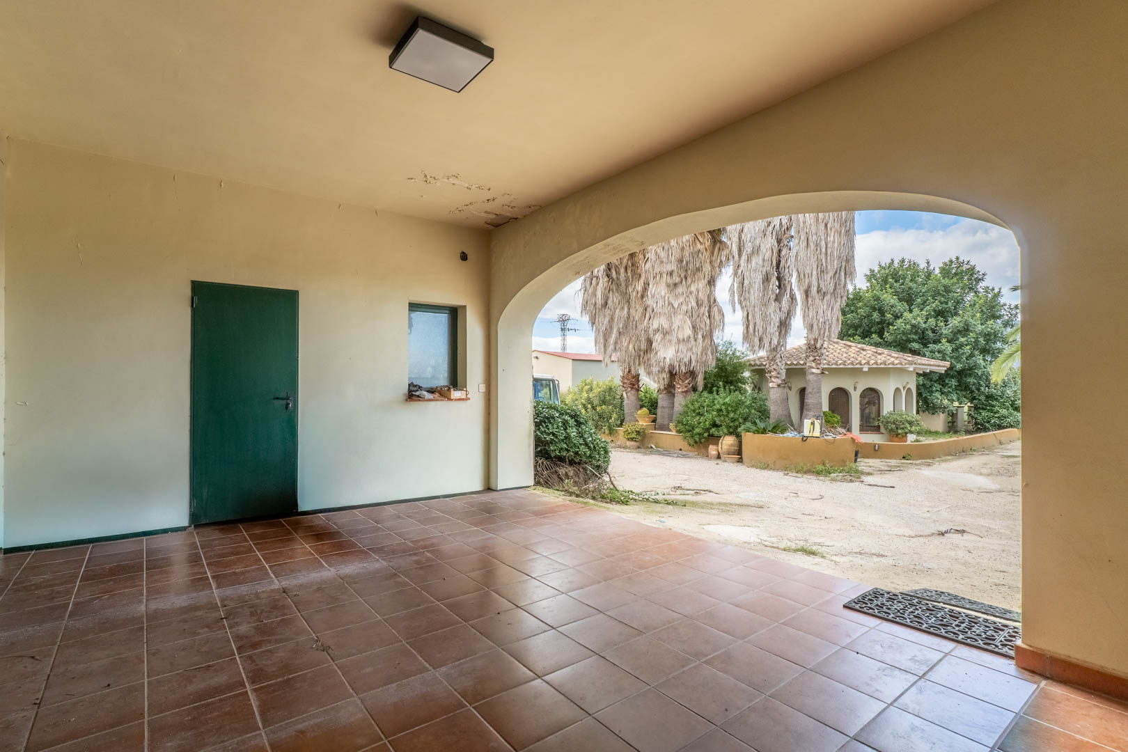 Covered porch featuring terracotta-style tiling and a wide archway overlooking the Mediterranean gardens and a separate guest house.