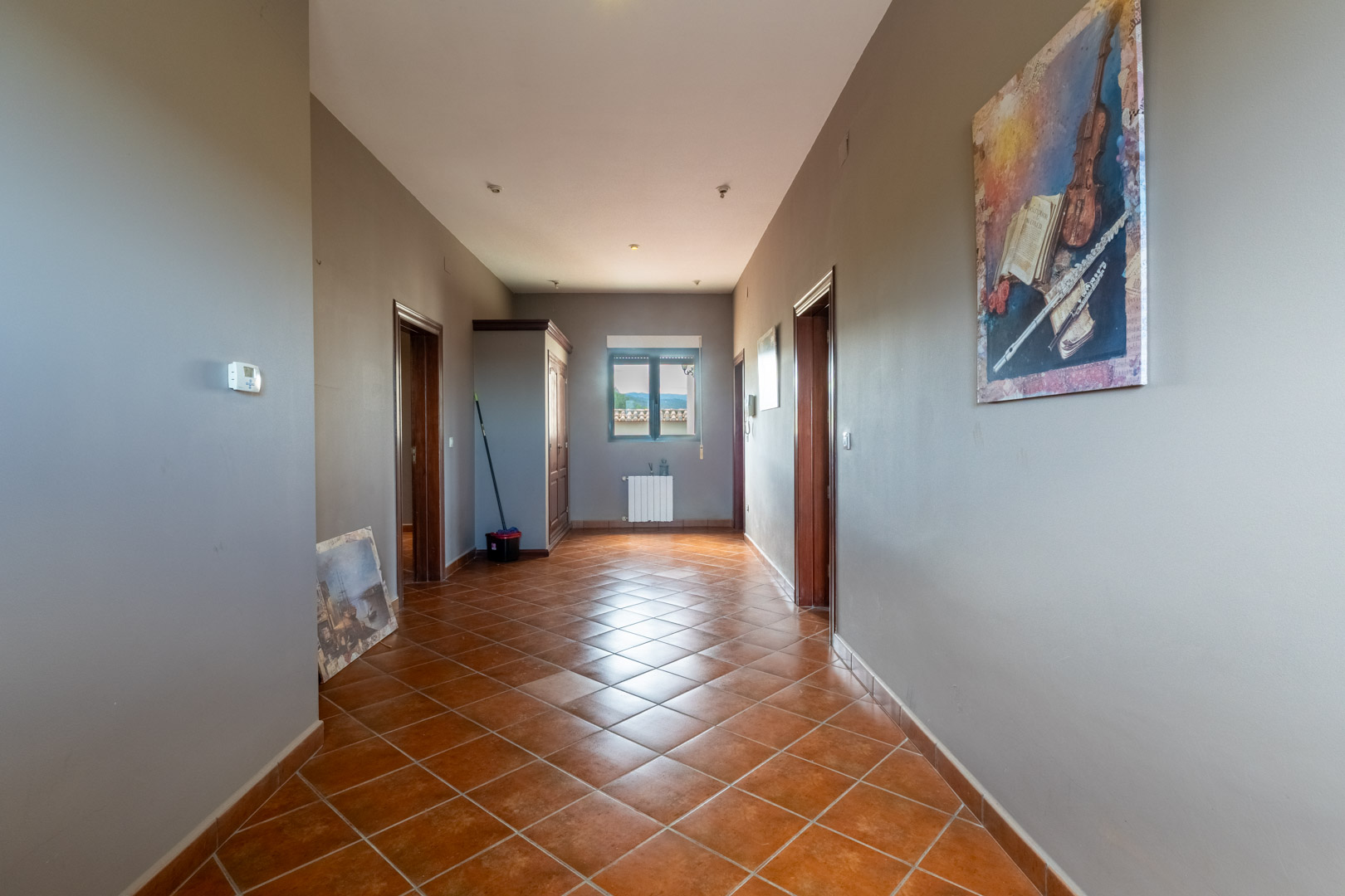 Distribution hallway featuring diagonal ceramic tile flooring, grey walls, and wooden door frames, lit by natural light and recessed ceiling spotlights.