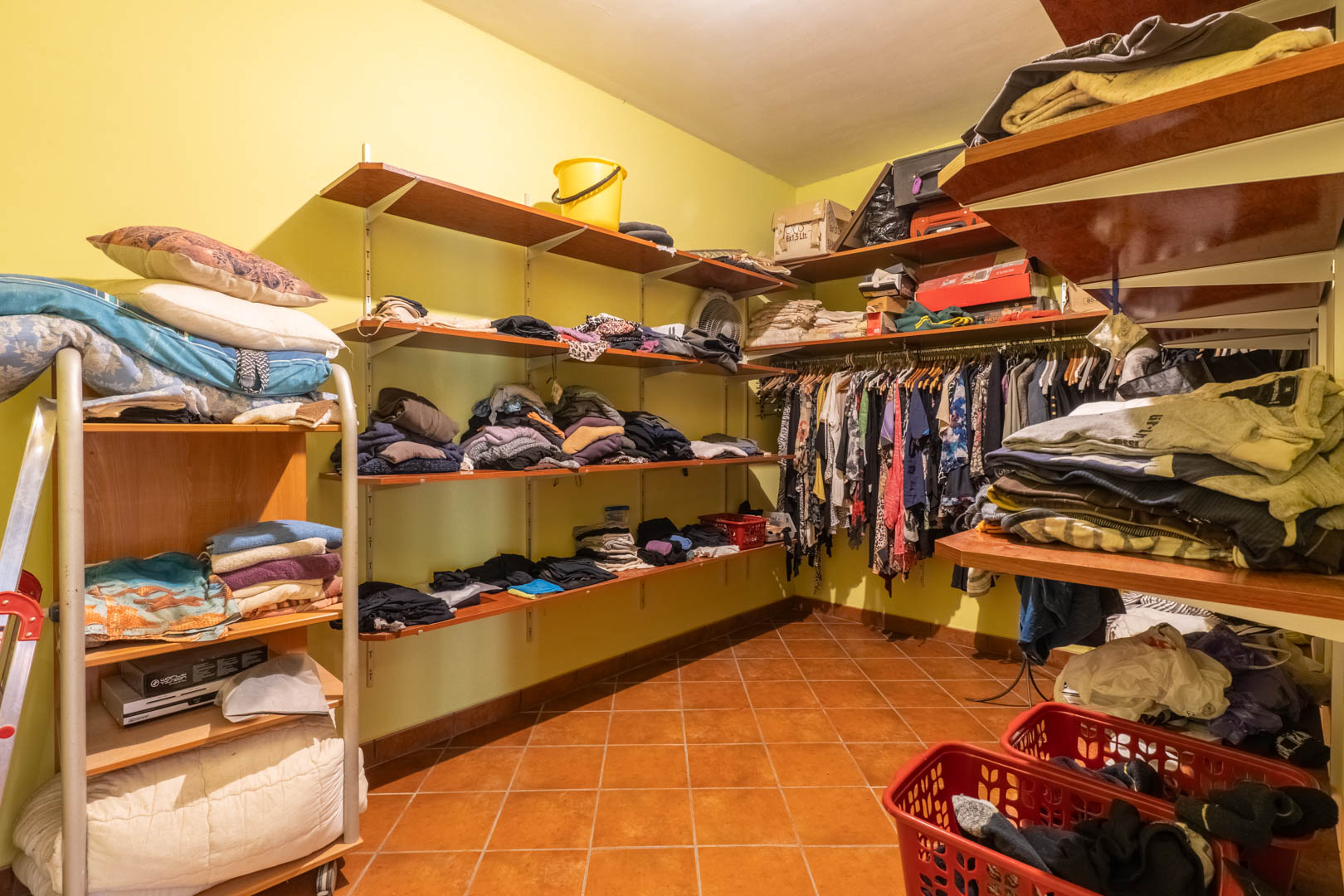 Functional walk-in closet featuring perimeter wooden shelving, garment rails, and rustic terracotta floor tiles, providing ample storage and organization space.