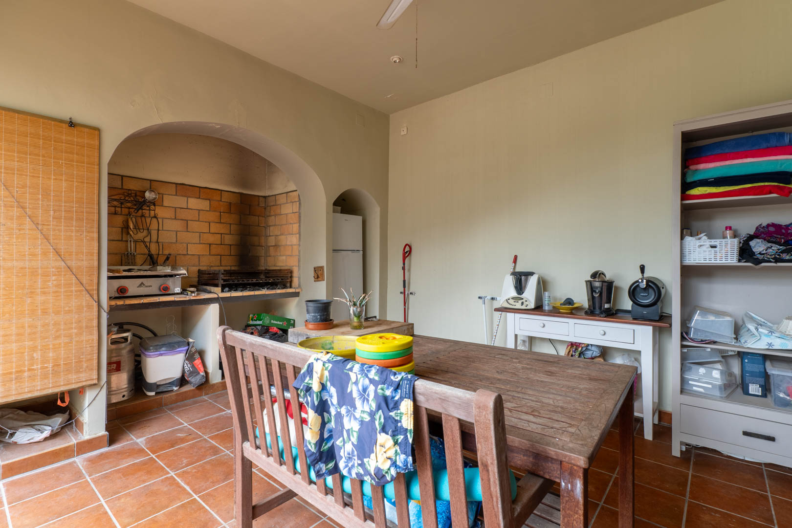 Outdoor kitchen area featuring a built-in brick barbecue, rustic wooden dining set, and traditional terracotta flooring.