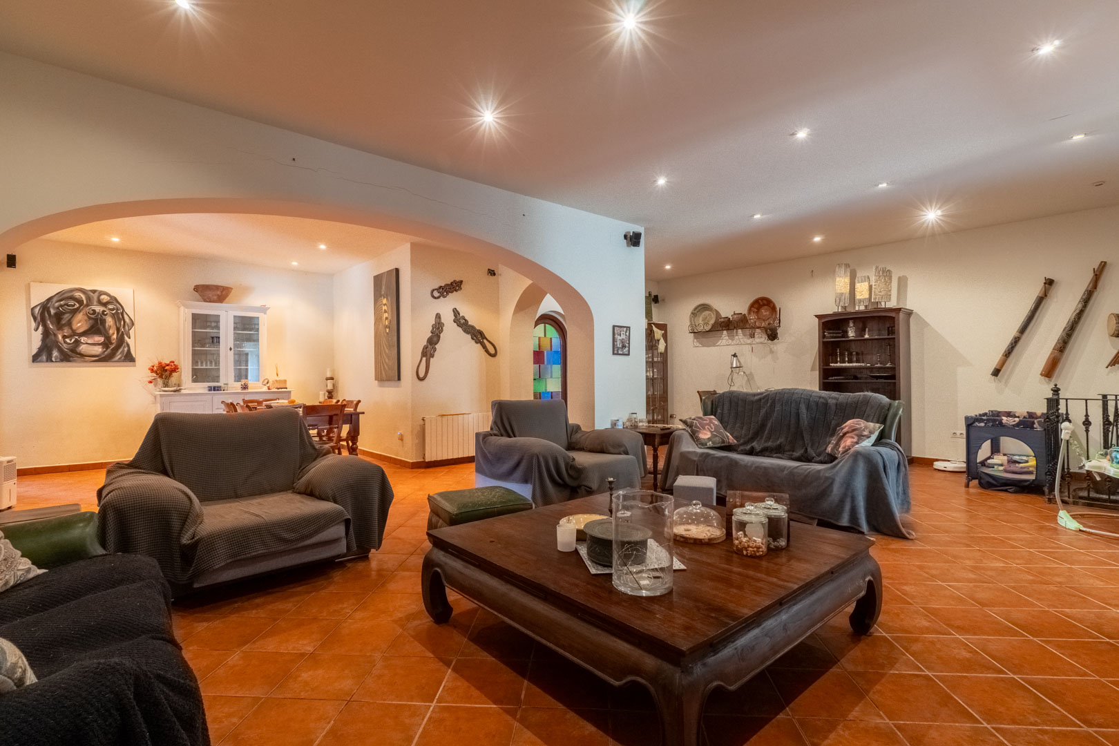 Spacious living area featuring terracotta tile flooring, recessed ceiling lighting, and a large architectural archway leading to the dining zone.