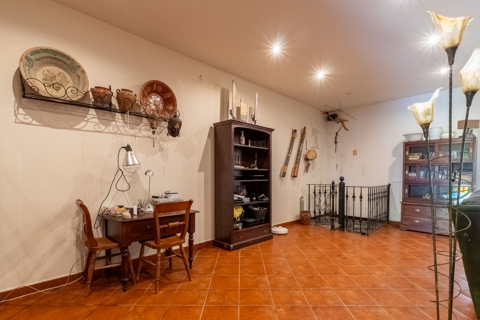Study area featuring a wooden desk, terracotta tile flooring, and a wrought iron railing overlooking the staircase to the lower level.