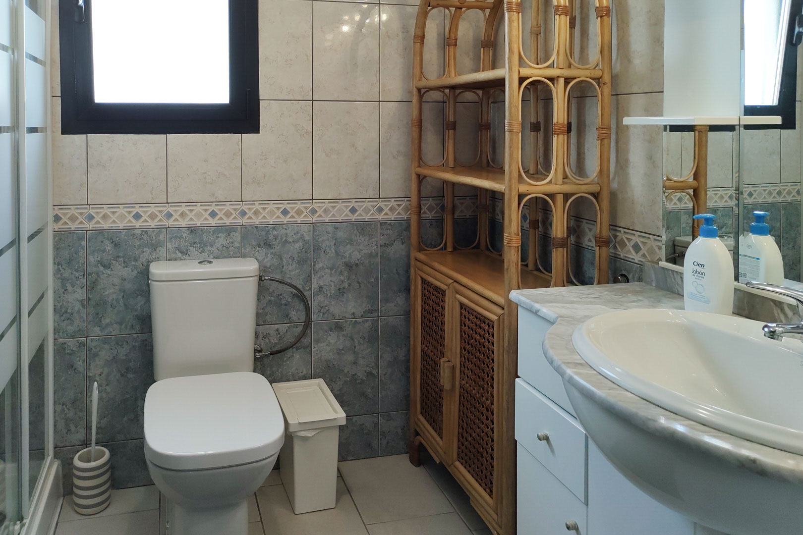Bathroom featuring a marble countertop, a bamboo storage unit, and two-tone wall tiling with a decorative border. Natural light enters through a side window.