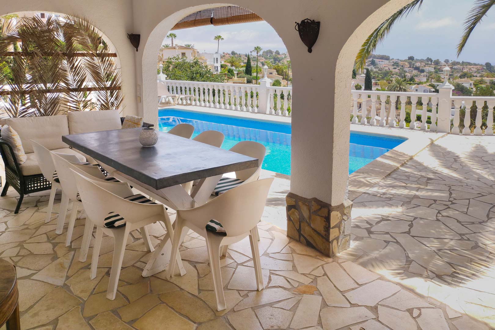 Covered terrace featuring traditional arches, natural stone flooring, and a dining area overlooking the swimming pool and scenic valley views.