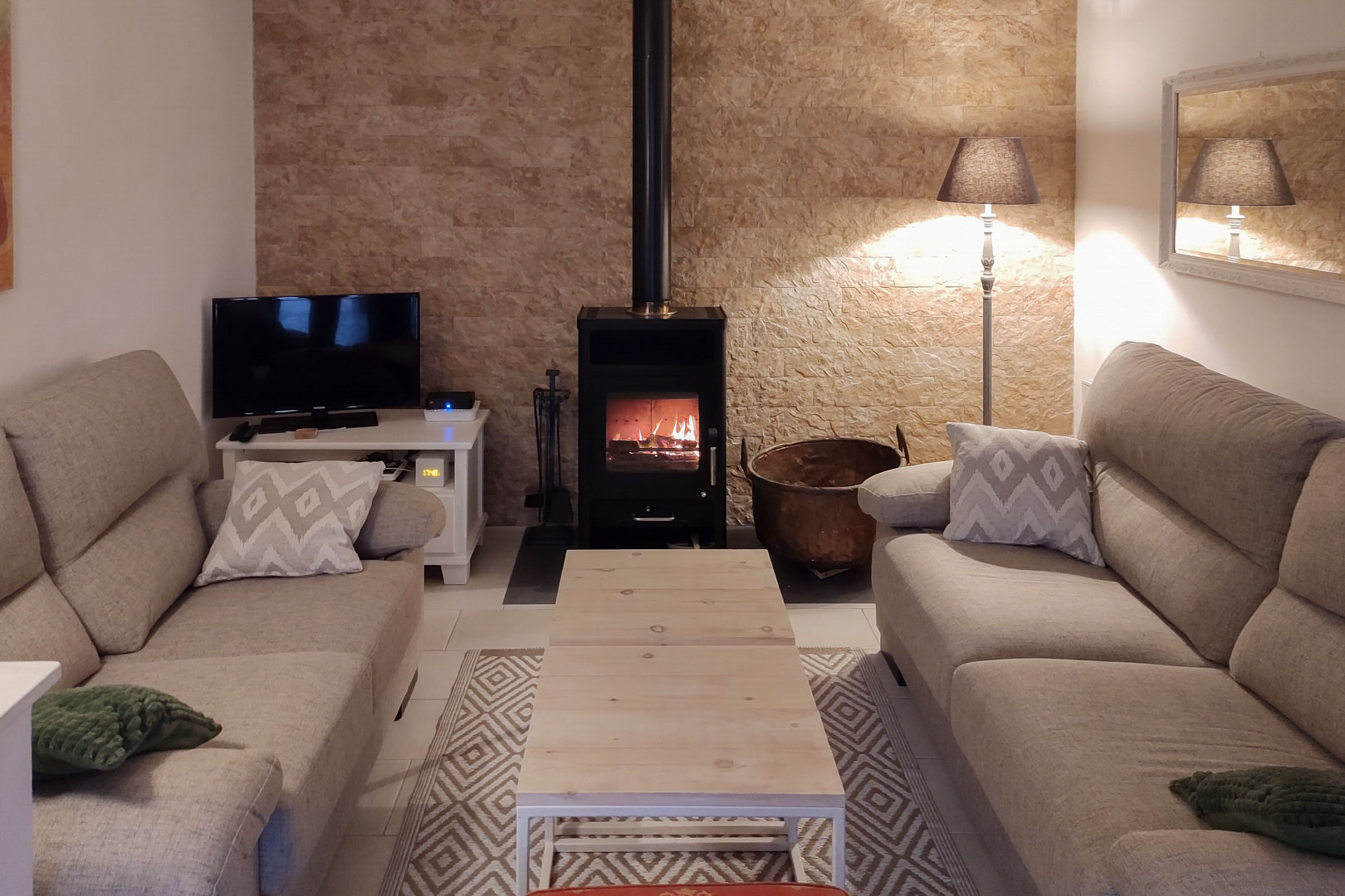Cozy living area featuring a black wood-burning stove set against a textured stone wall, complemented by neutral sofas and a light wood coffee table.