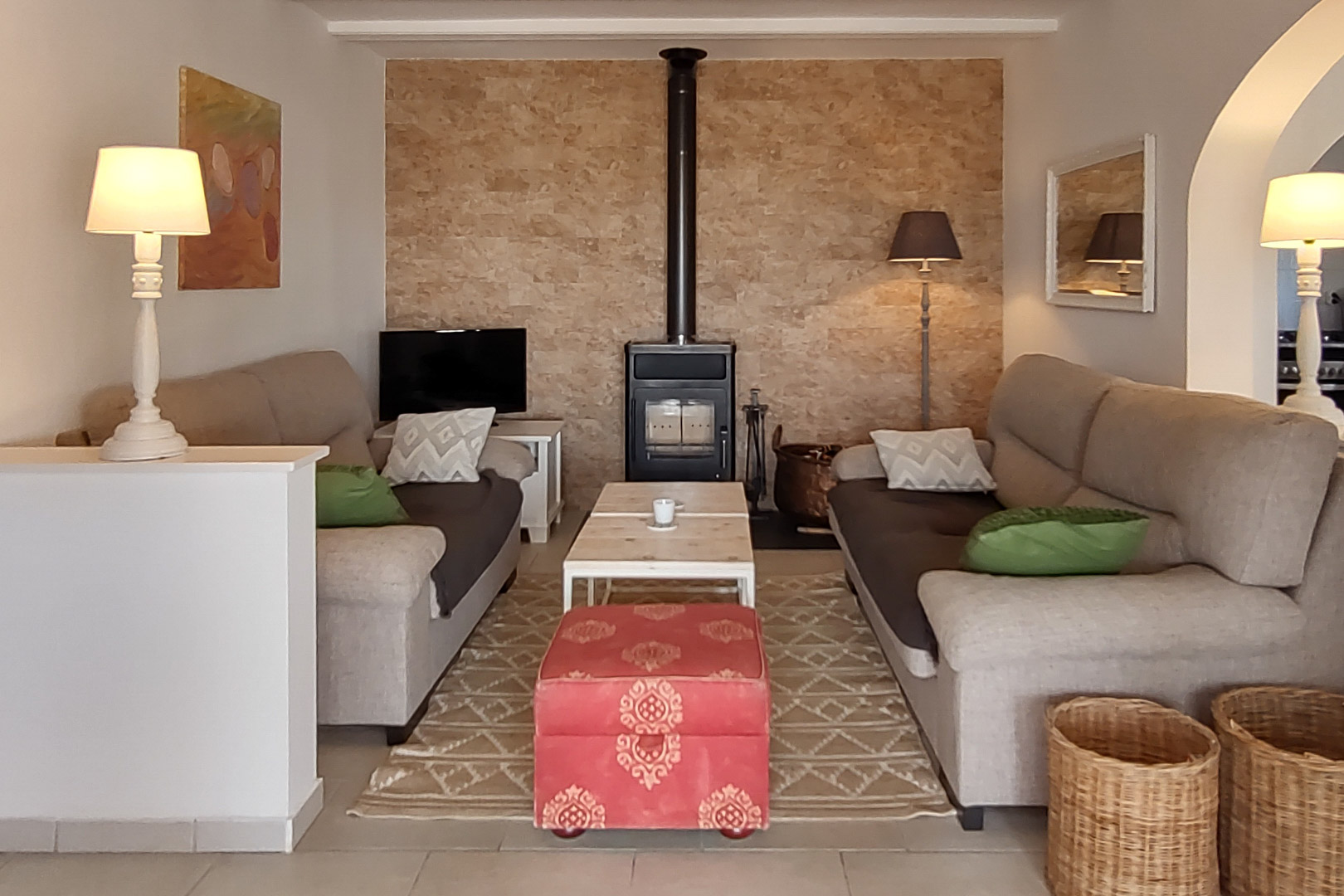 Cozy living room featuring a wood-burning stove against a natural stone accent wall, twin sofas, a wooden coffee table, and a decorative red ottoman.