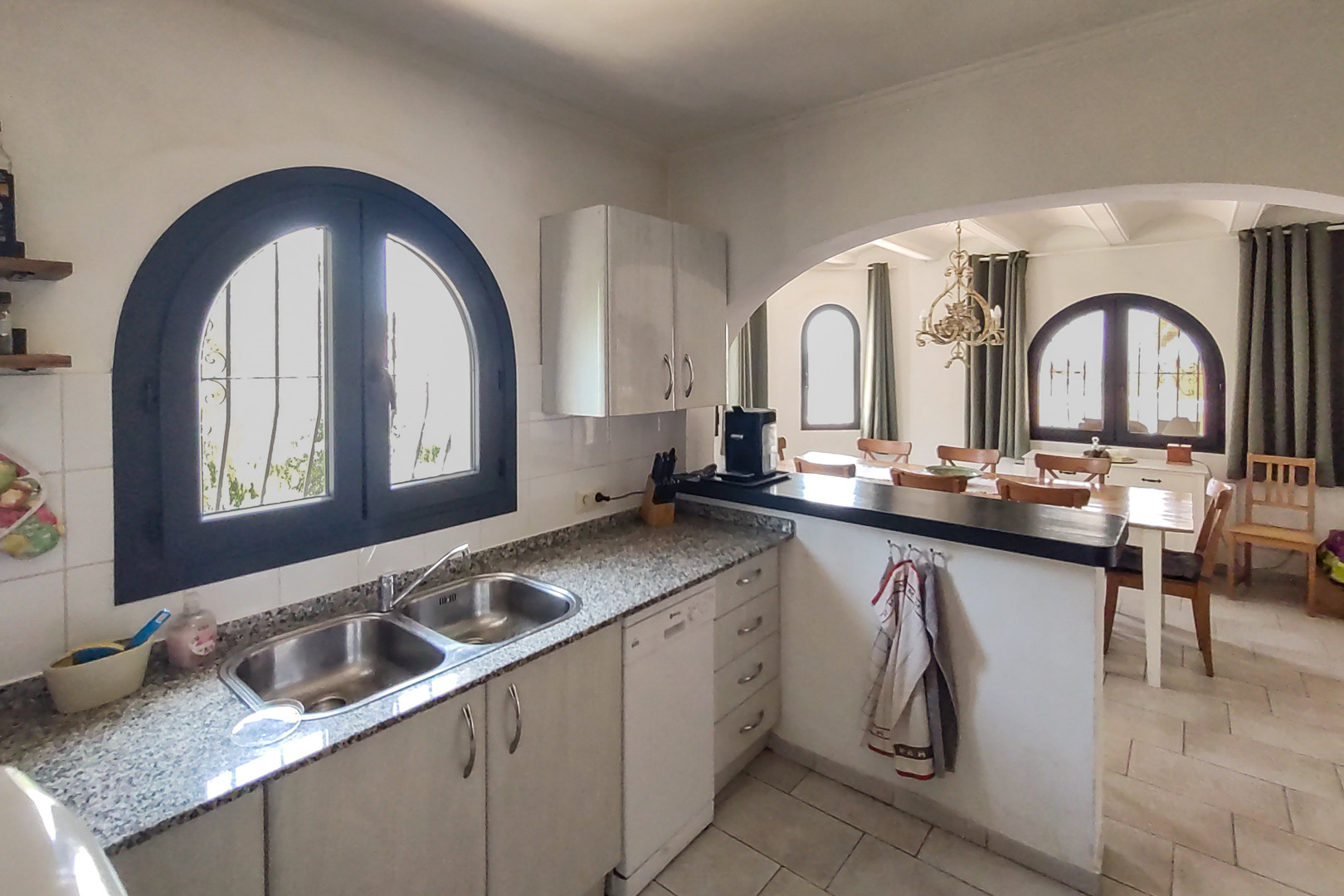 Fully equipped kitchen with granite countertops and double sink, opening to the dining area through an arch. Features a dishwasher and a traditional arched window.