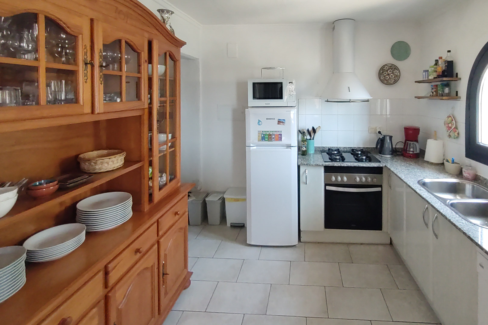 Functional kitchen featuring granite countertops, gas hob, and a large solid wood dresser for storage, set on neutral tiled flooring.