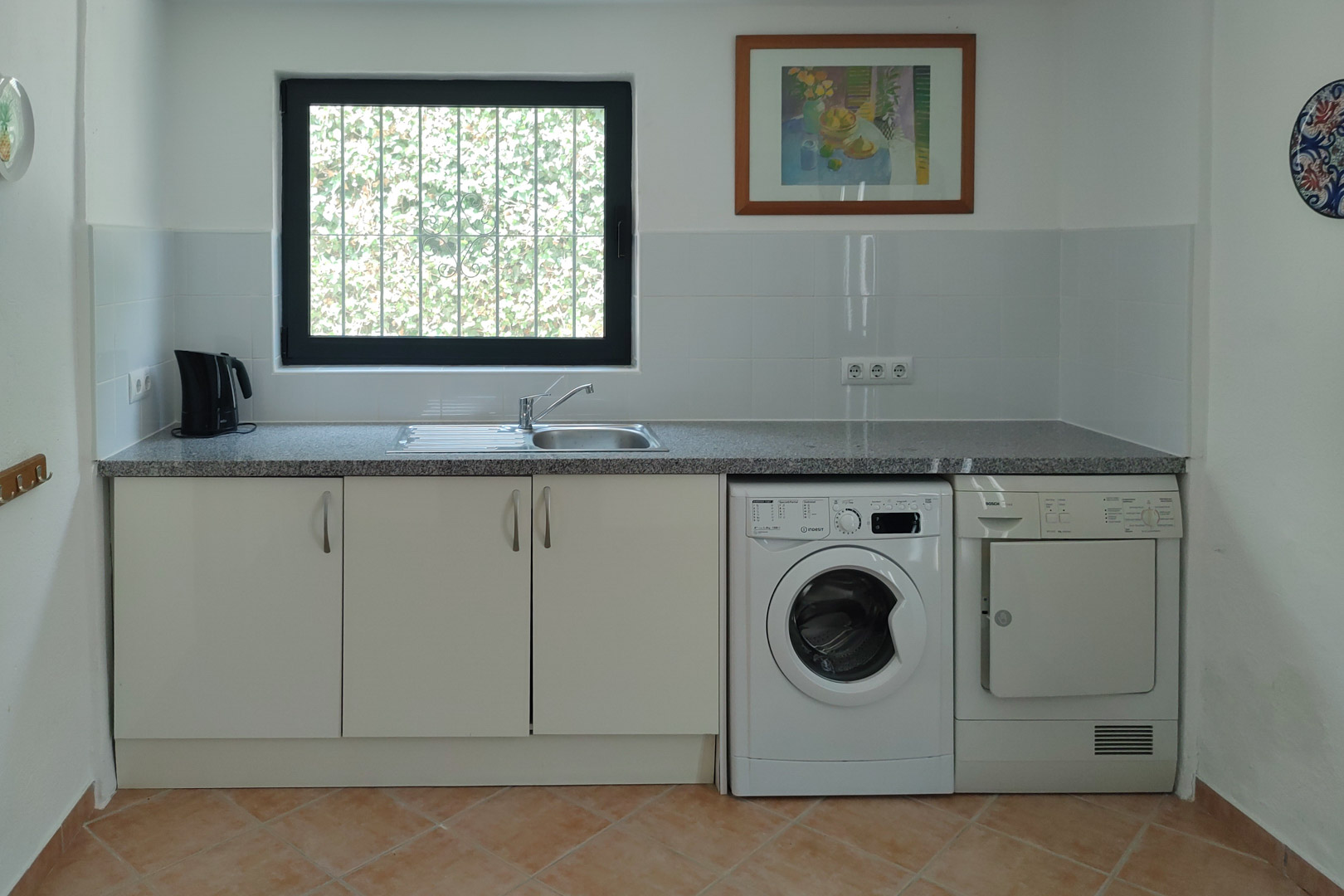 Functional laundry area featuring a granite countertop, stainless steel sink, integrated washing machine and dryer, white cabinetry, and tiled flooring.