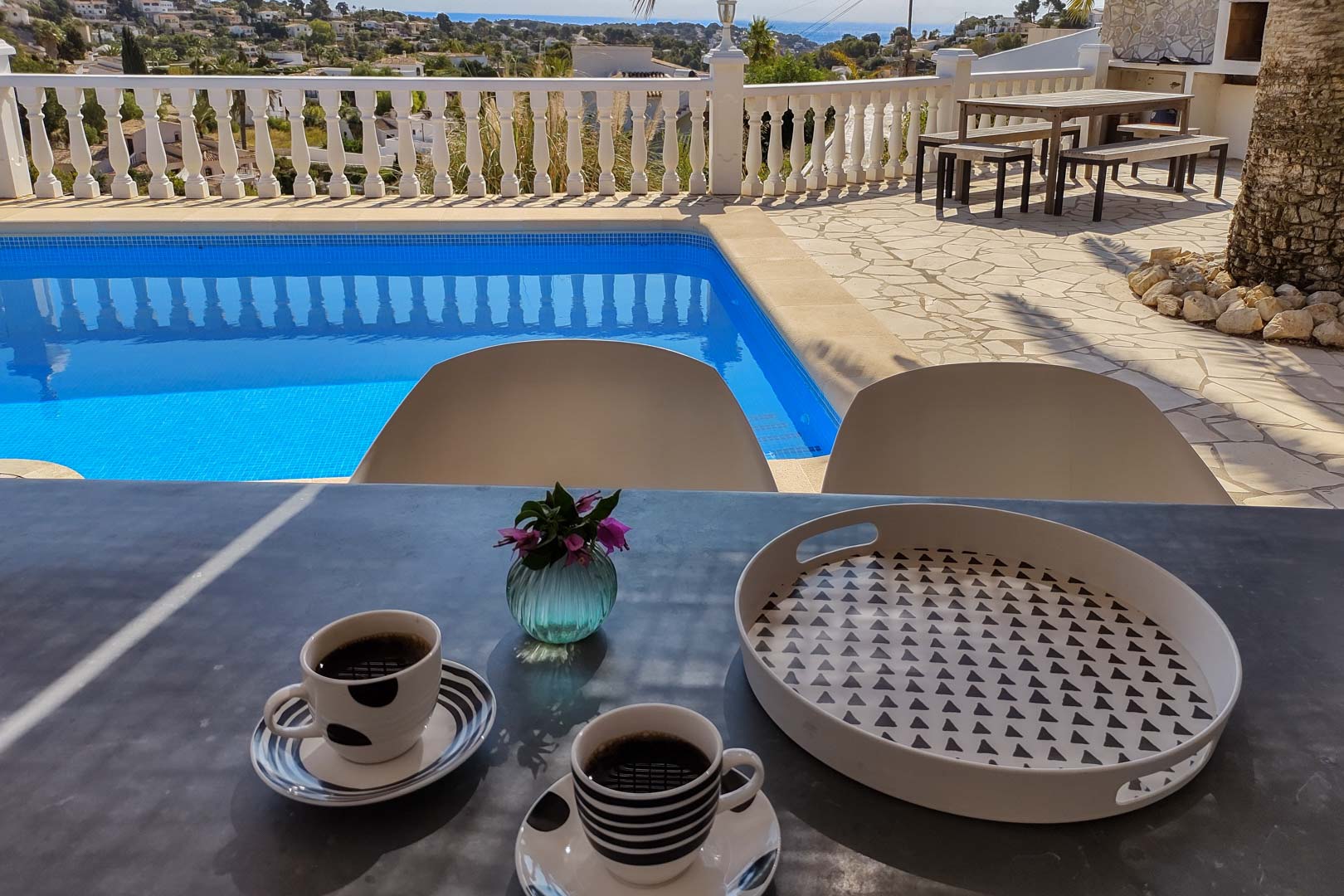 Main terrace featuring a private pool and sea views. Includes an outdoor dining area with a wooden table and benches set on natural stone paving with a white balustrade.