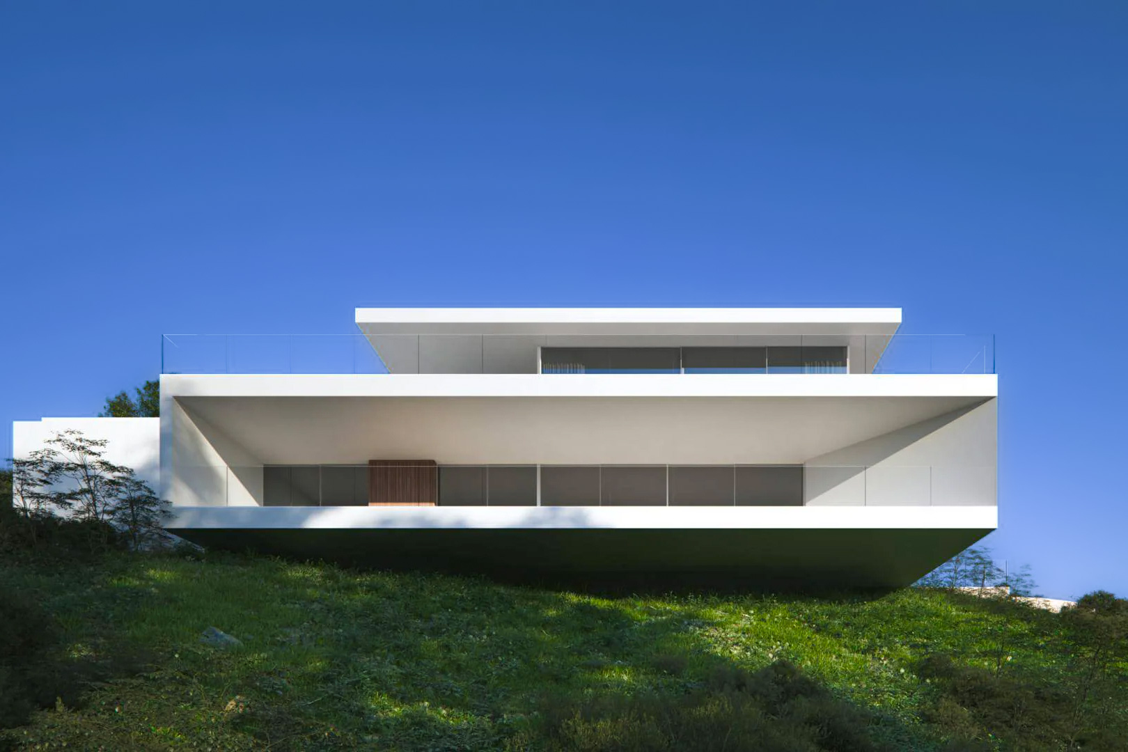 Avant-garde facade featuring pure white lines and cantilevered volumes, with expansive glass terraces integrated into the natural hillside of Moraira.