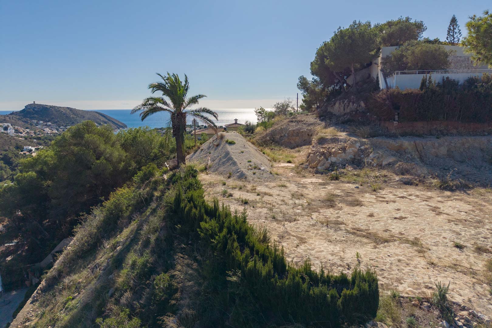 Elevated building plot in Moraira featuring panoramic Mediterranean Sea views and El Portet coastline, set amidst native pine trees and natural surroundings.