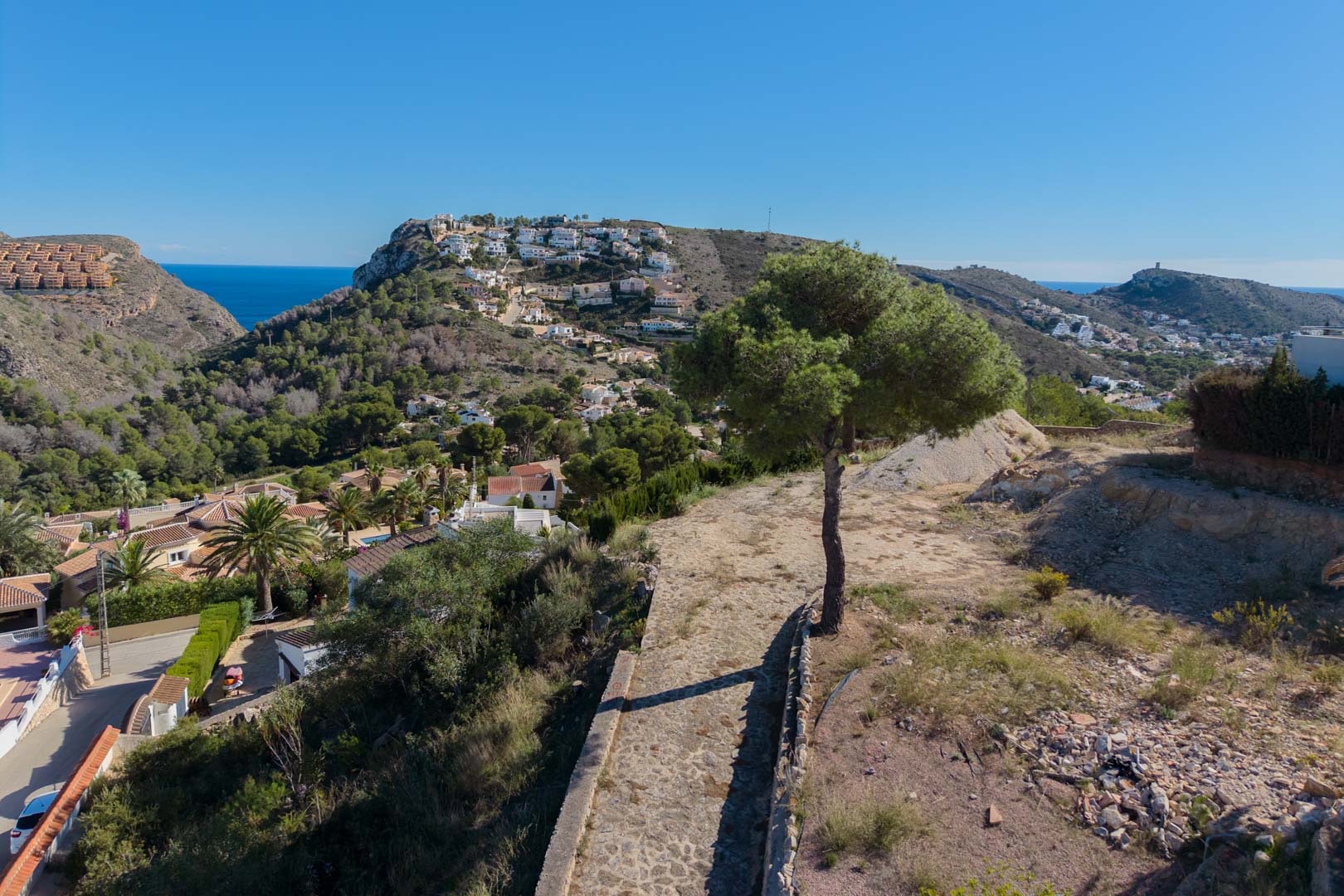 Elevated panoramic views overlooking the Moraira valley and the Mediterranean Sea, featuring native pine trees and coastal hillsides.
