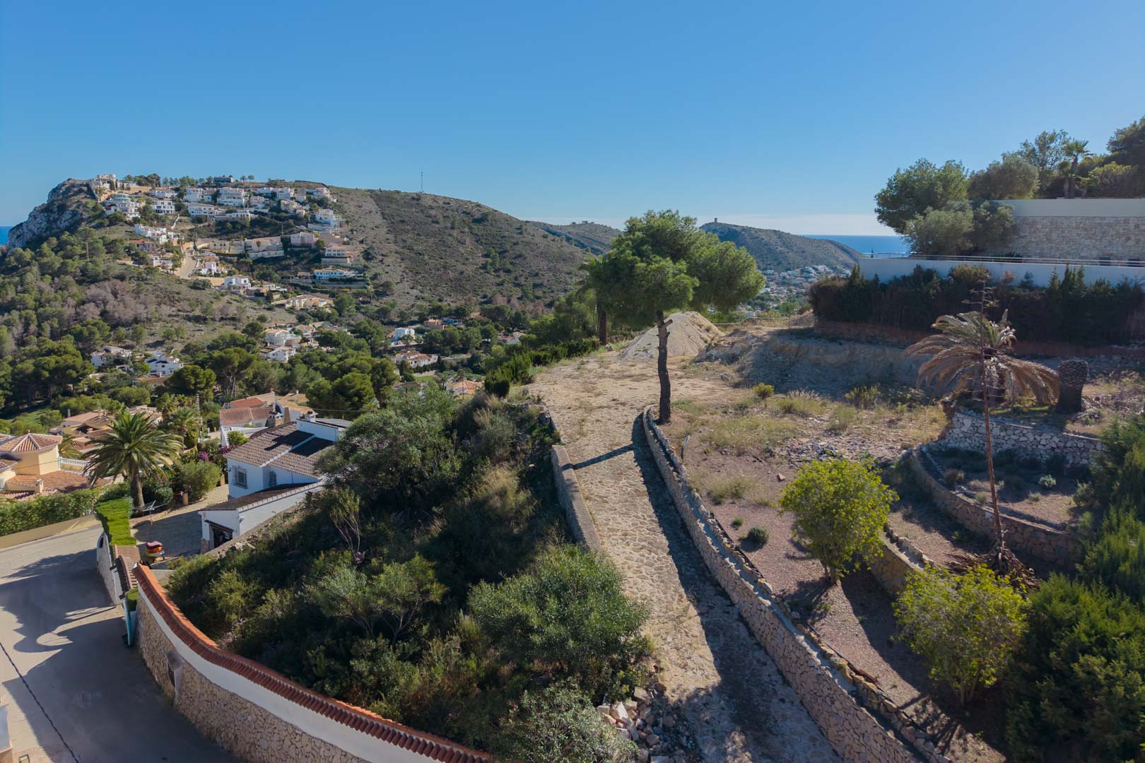 Elevated view of the plot featuring natural stone masonry walls and Mediterranean vegetation, with panoramic views of the valley and the sea in Moraira.