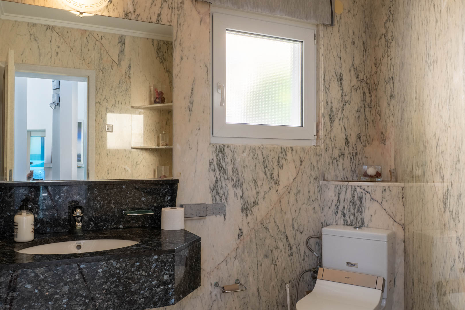 Bathroom featuring veined marble walls and a black granite countertop.