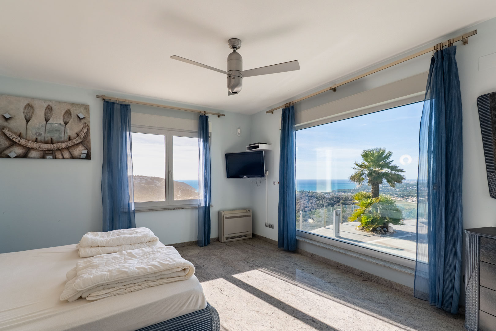 Bright bedroom featuring granite floors, blue curtains, and sea views through large windows.