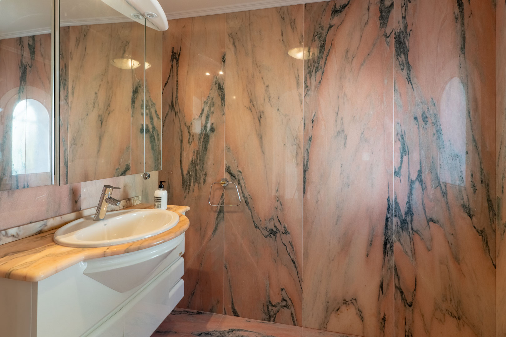 Bathroom featuring full-height pink marble wall cladding with dark veining. It includes a matching stone countertop, white vanity, and a large mirror reflecting natural light.