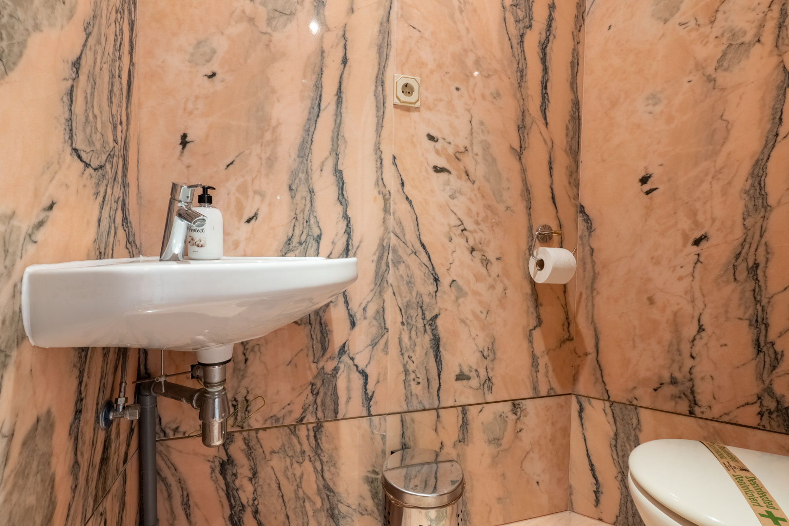 Guest toilet featuring full-height pink marble wall cladding with dark veining, a wall-mounted ceramic sink, and chrome fixtures.