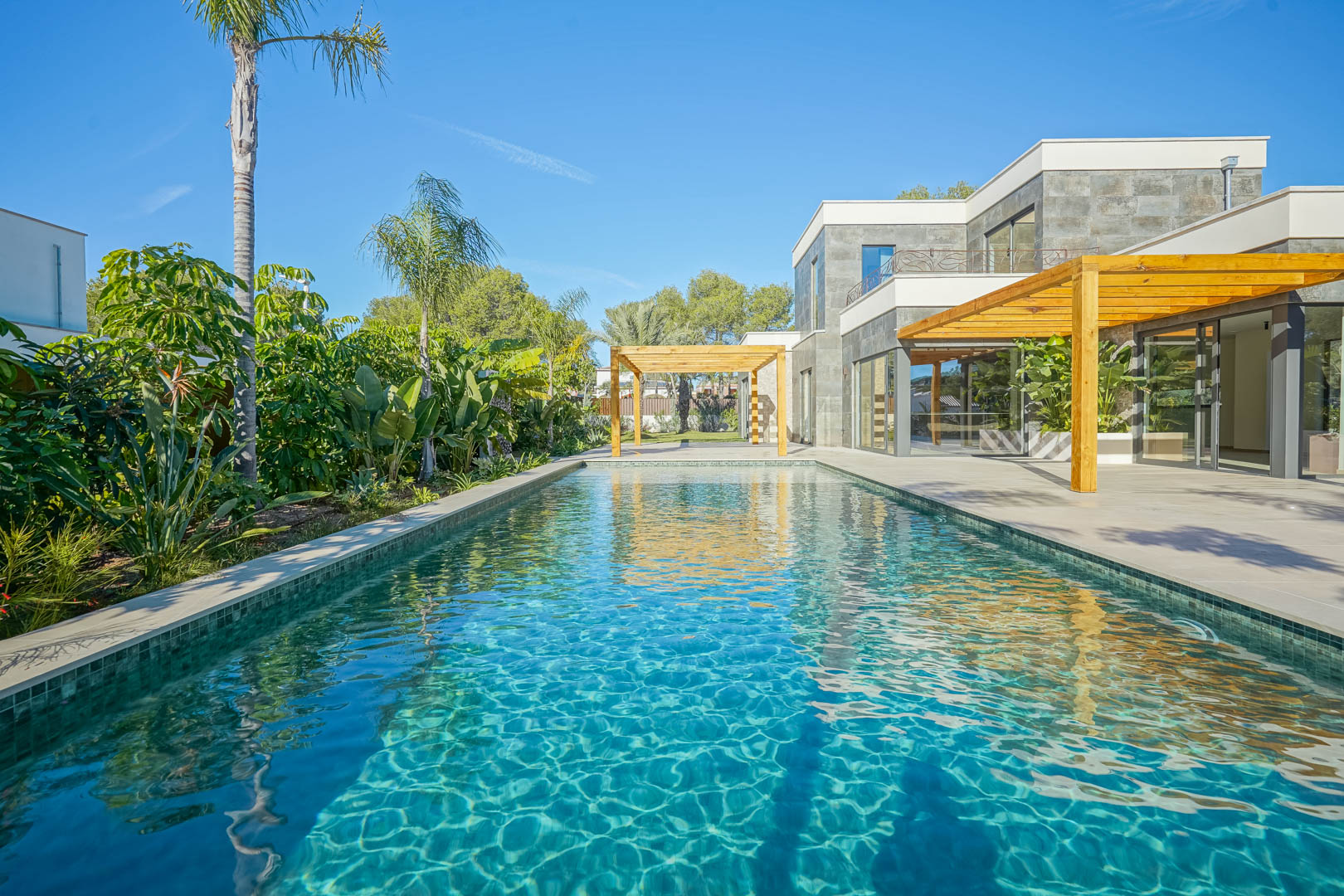 Bali-style pool with emerald tiling, featuring a spacious terrace with iroko wood pergolas and a lush Mediterranean garden with palm trees.