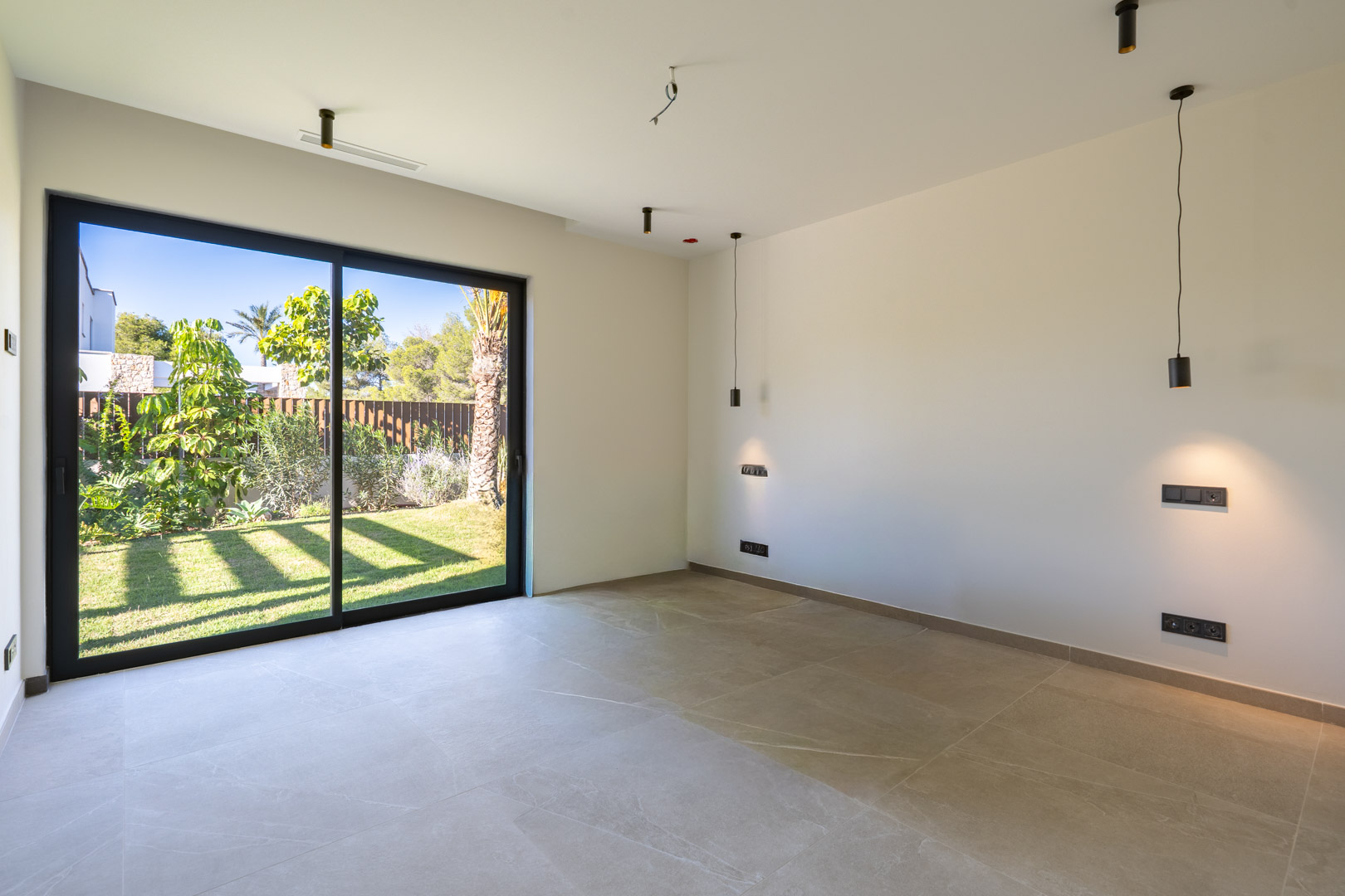 Bedroom featuring porcelain tile floors and large sliding doors with direct garden access. Includes minimalist black pendant lights and integrated air conditioning.