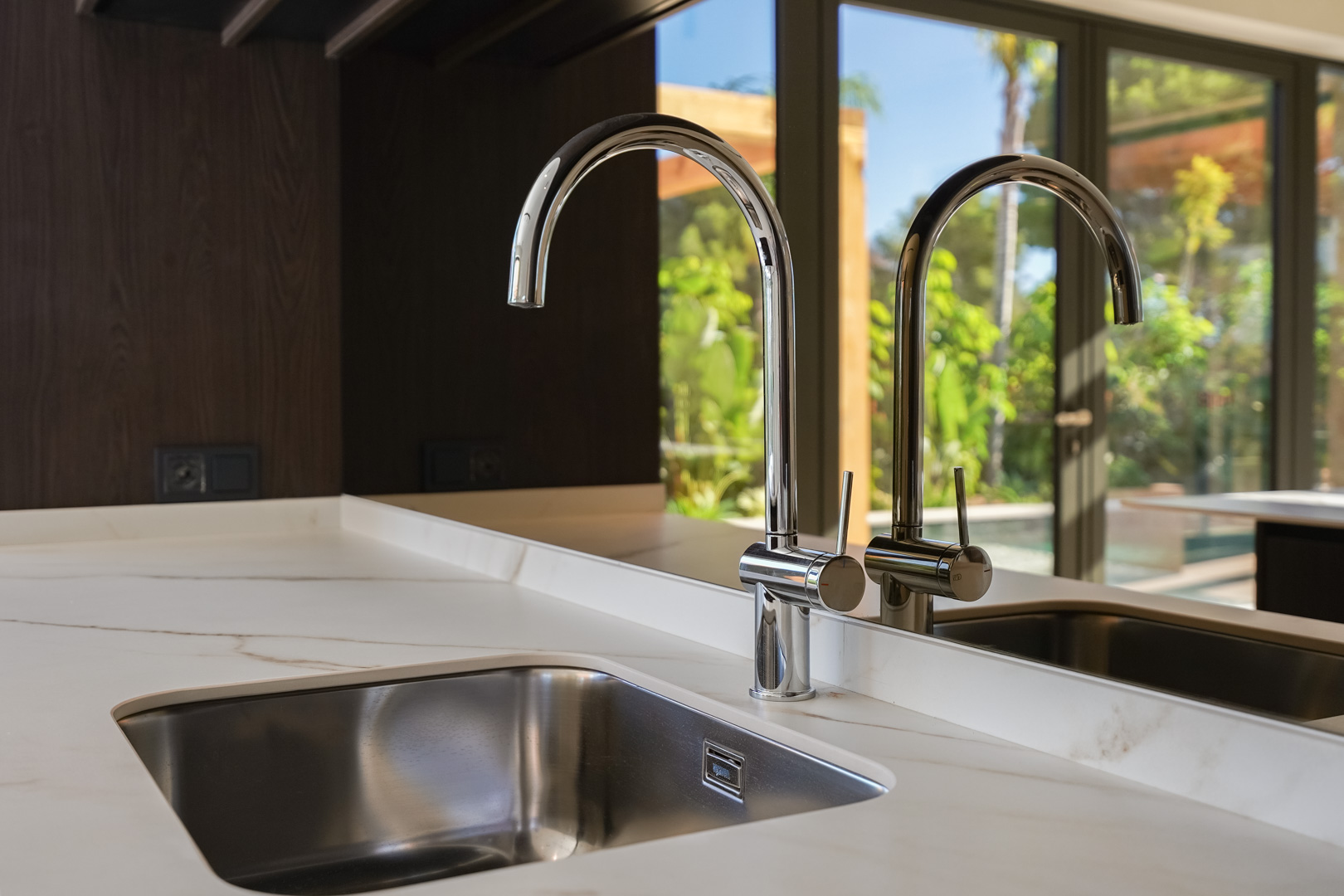 Close-up of an undermount stainless steel sink with a high-arc chrome faucet set into a white veined marble countertop.