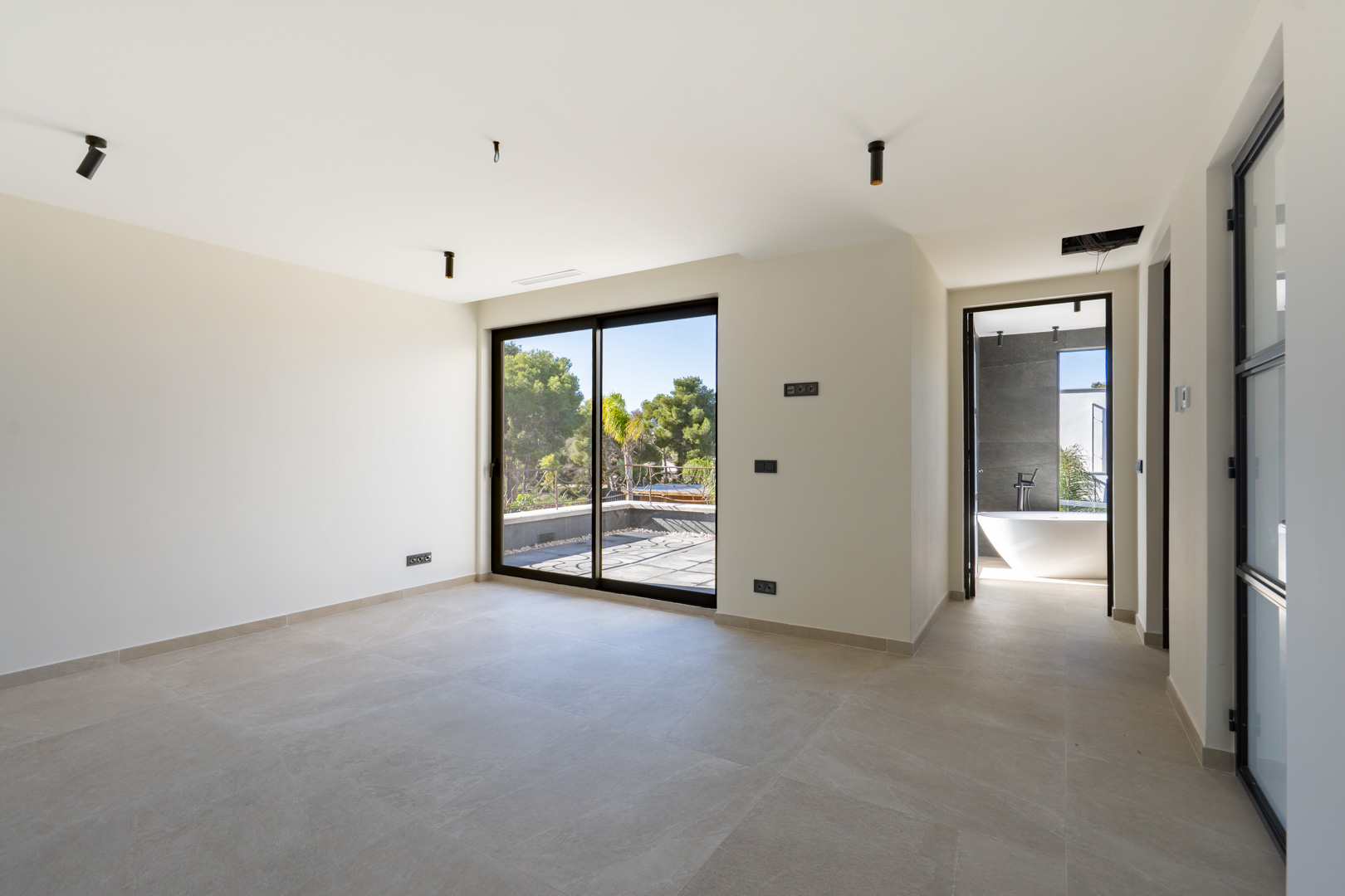 Master bedroom featuring a private terrace, large-format tiled flooring, and an en-suite bathroom with a freestanding bathtub and dark stone-effect walls.