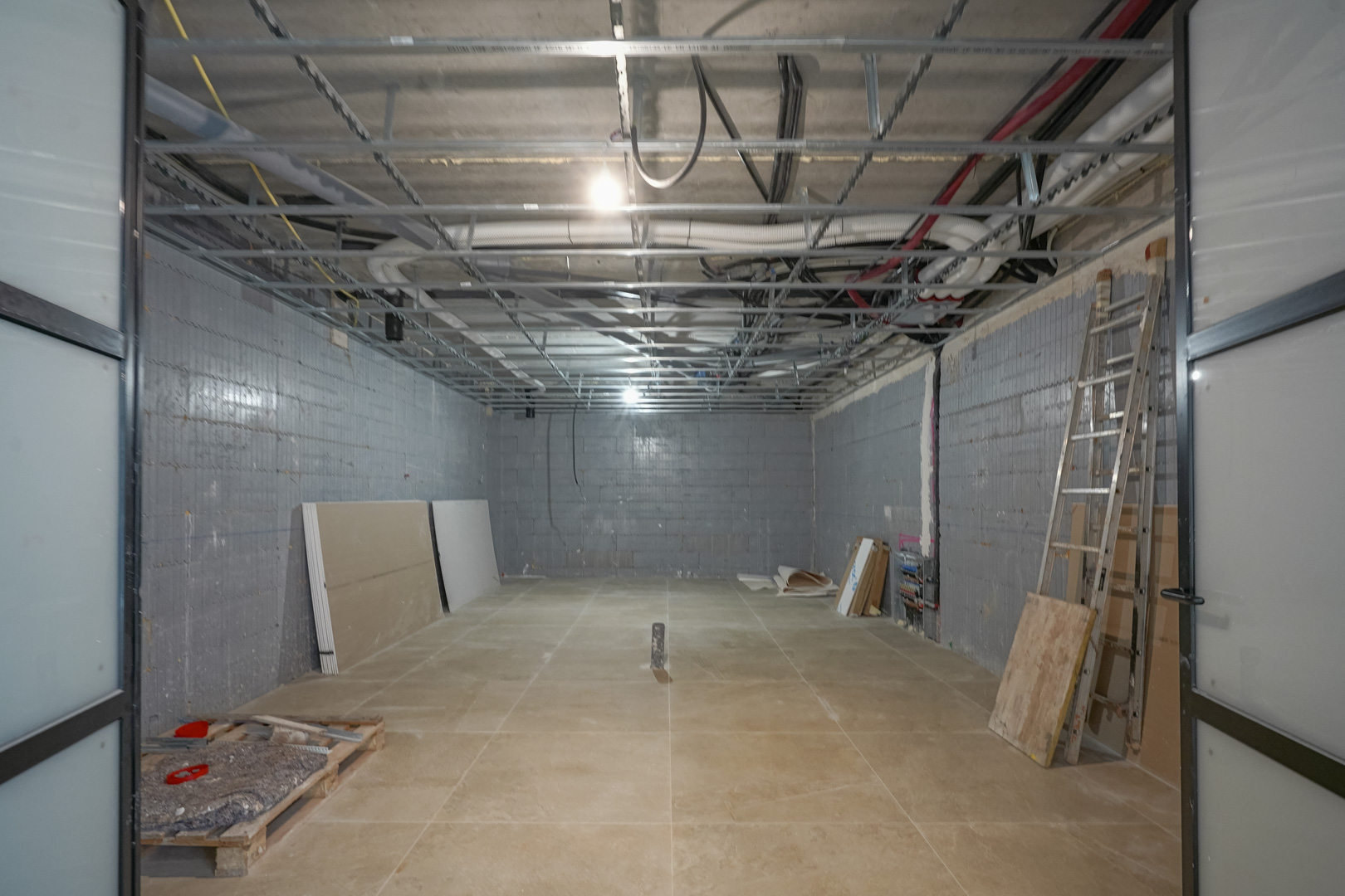 Spacious 180 m2 basement under construction featuring insulated Styro Stone walls, exposed ceiling installations, and large black-framed sliding doors.