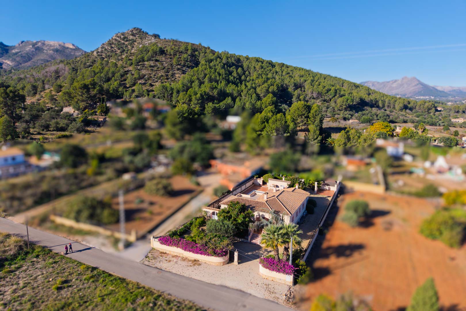 Aerial perspective of the Mediterranean villa on a flat plot, showing the terracotta roof and bougainvillea gardens against a mountain landscape.