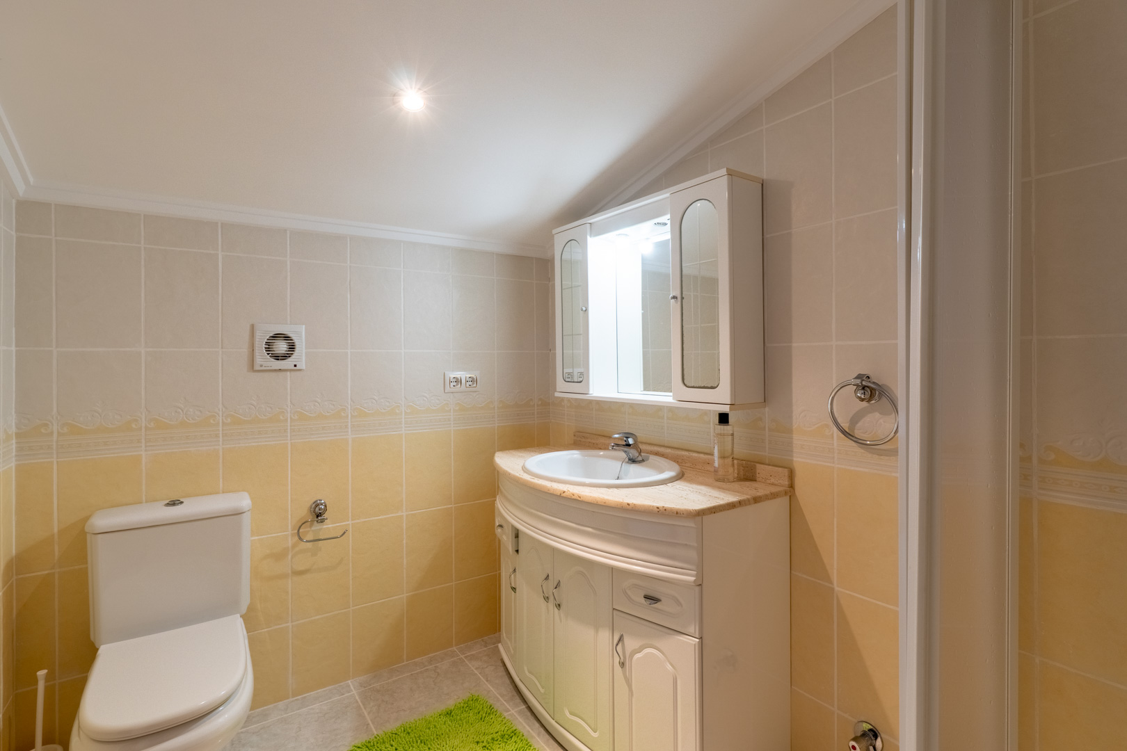Bathroom featuring cream and yellow tiling, a curved vanity unit with a marble countertop, and a mirrored wall cabinet with integrated lighting.