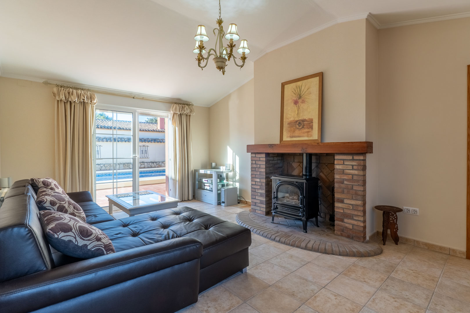Bright living room featuring a brick fireplace with a wood-burning stove, leather seating, and direct access to the outdoor pool area.