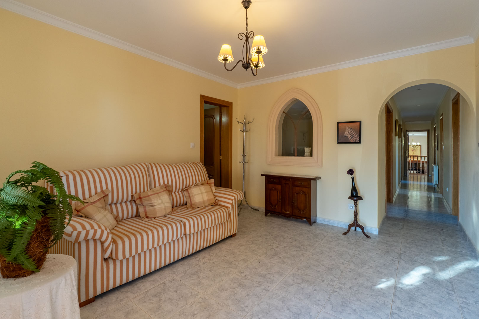 Distribution hall featuring ceramic tile flooring, a striped sofa, and an arched doorway. A decorative pointed arch interior window adds a traditional touch.