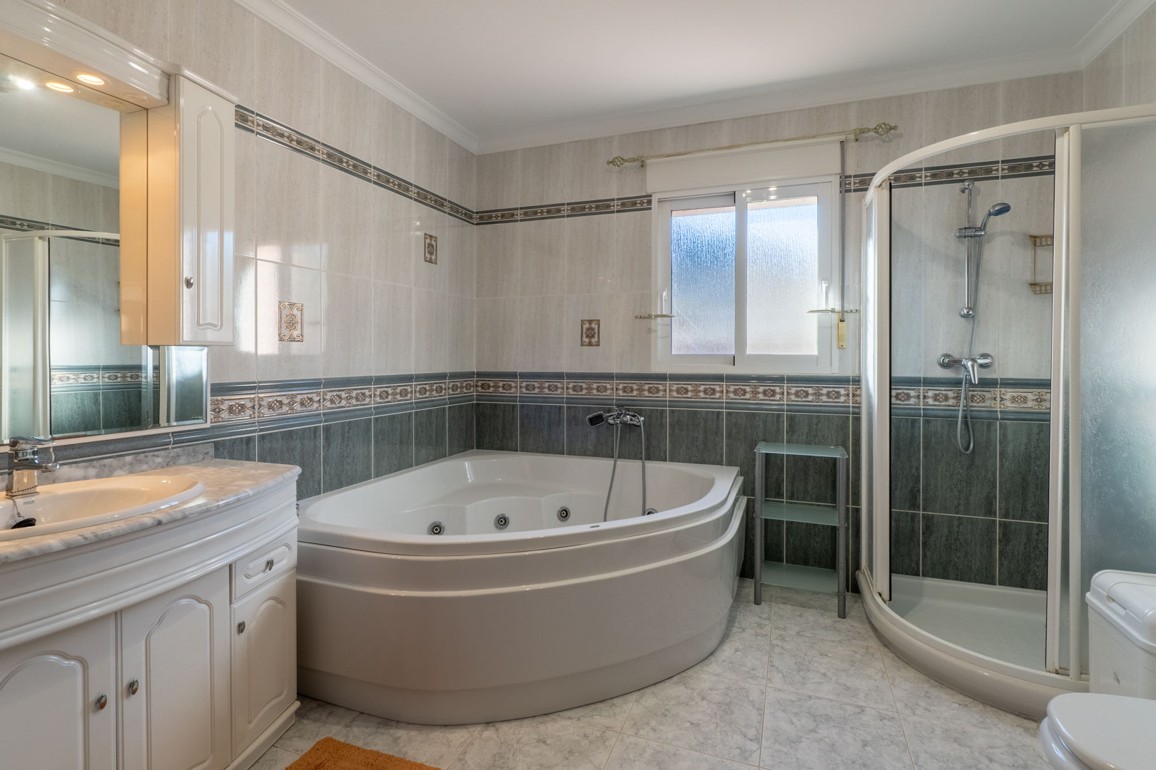 Full bathroom featuring a corner whirlpool tub, separate curved glass shower, and vanity with marble countertop and integrated storage.