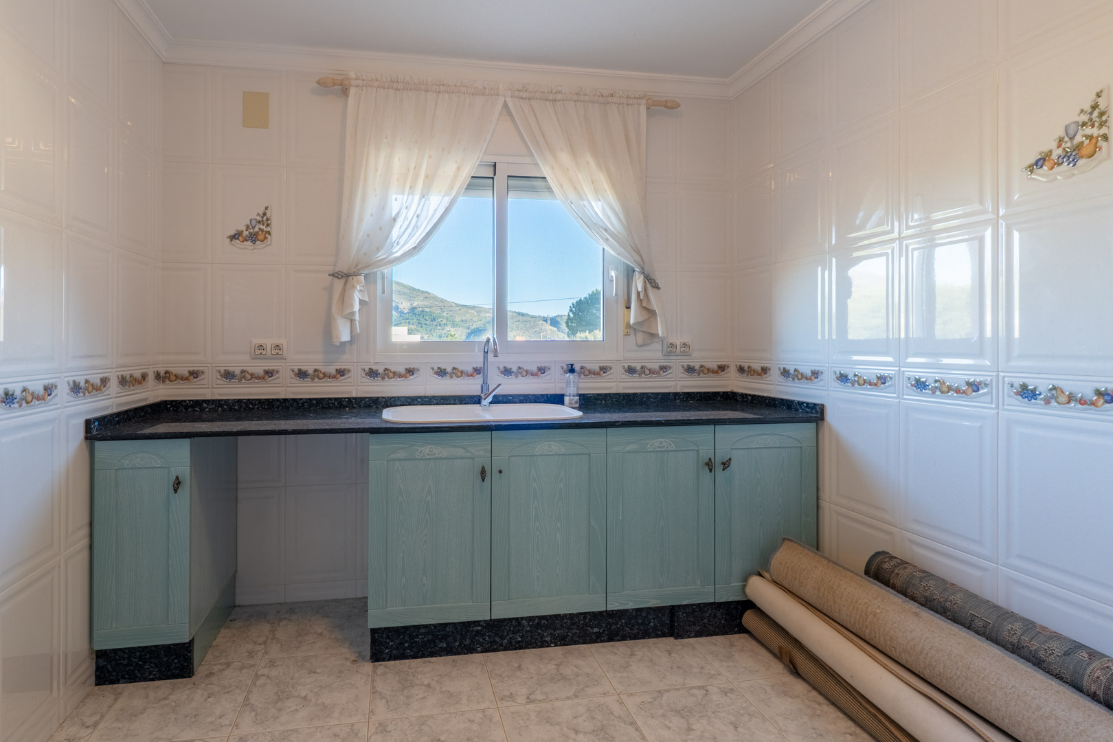 Functional kitchen featuring light blue wooden cabinetry, dark granite countertops, and a window overlooking the scenic Jalón valley mountains.