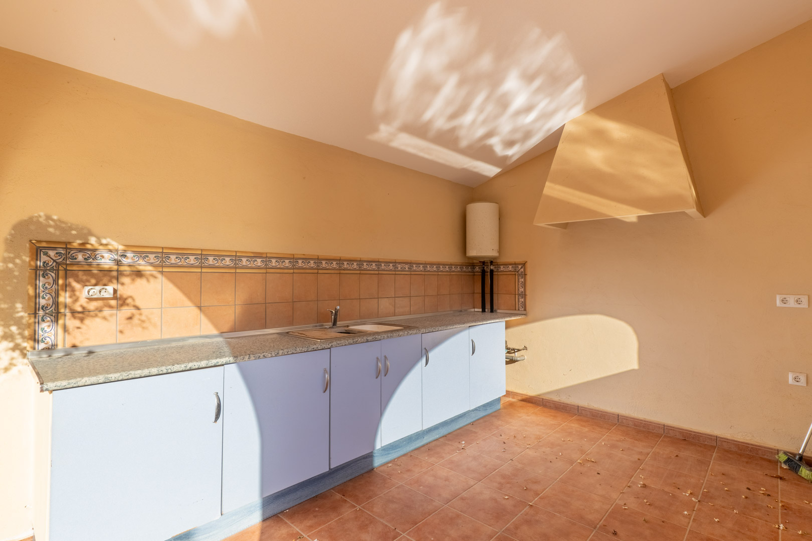 Functional outdoor kitchen featuring a granite countertop, light blue cabinetry, and traditional tiled backsplash. Equipped with a stainless steel sink and a large extractor hood.