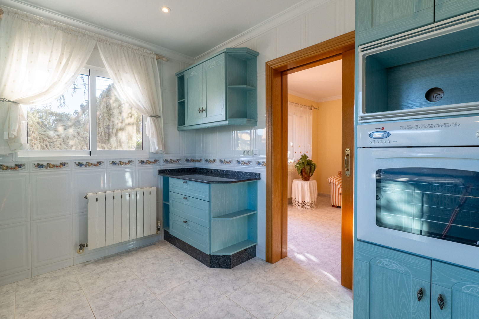 Independent kitchen featuring light blue cabinetry, dark granite countertops, white tiled walls, and a wooden doorway connecting to the living area.