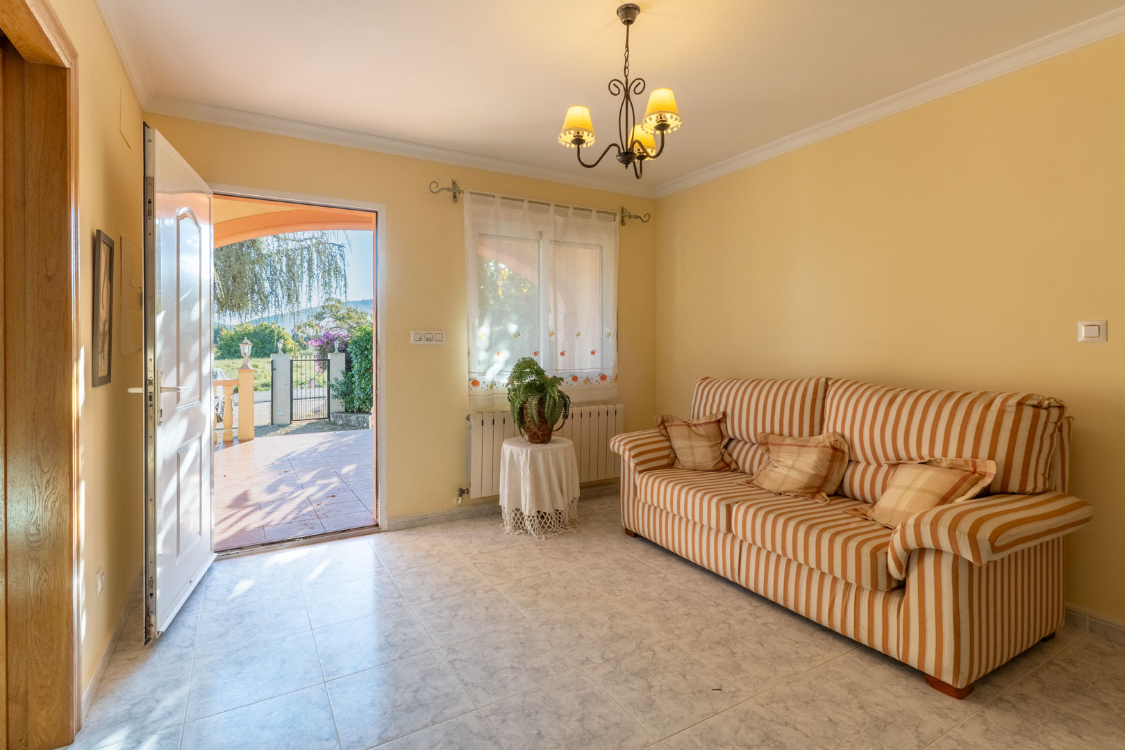 Independent lounge with direct outdoor access, featuring a striped sofa, light tile flooring, and natural light from the entrance.