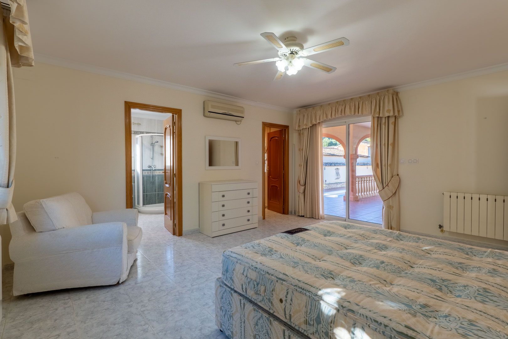Master bedroom featuring an en-suite bathroom, air conditioning, and direct access to the terrace. It includes light tiled flooring, a ceiling fan, and pool area views.