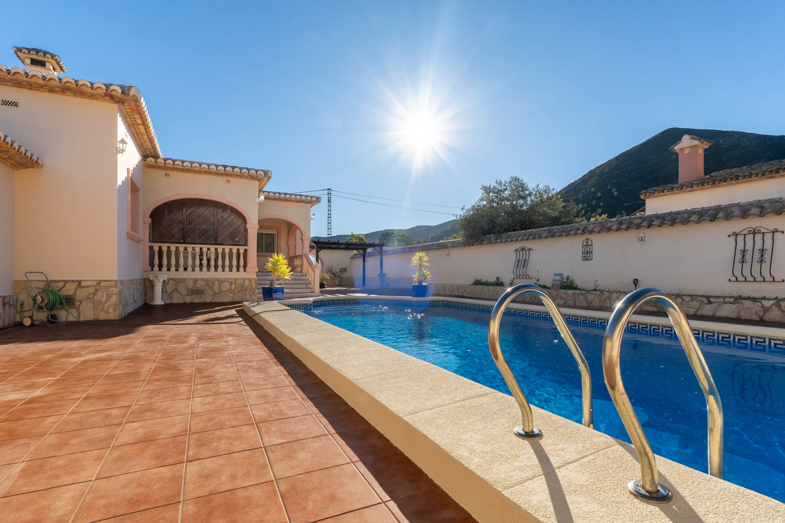 Private swimming pool featuring a Greek key border, surrounded by a terracotta tiled terrace with views of the Jalón valley mountains under a clear sky.
