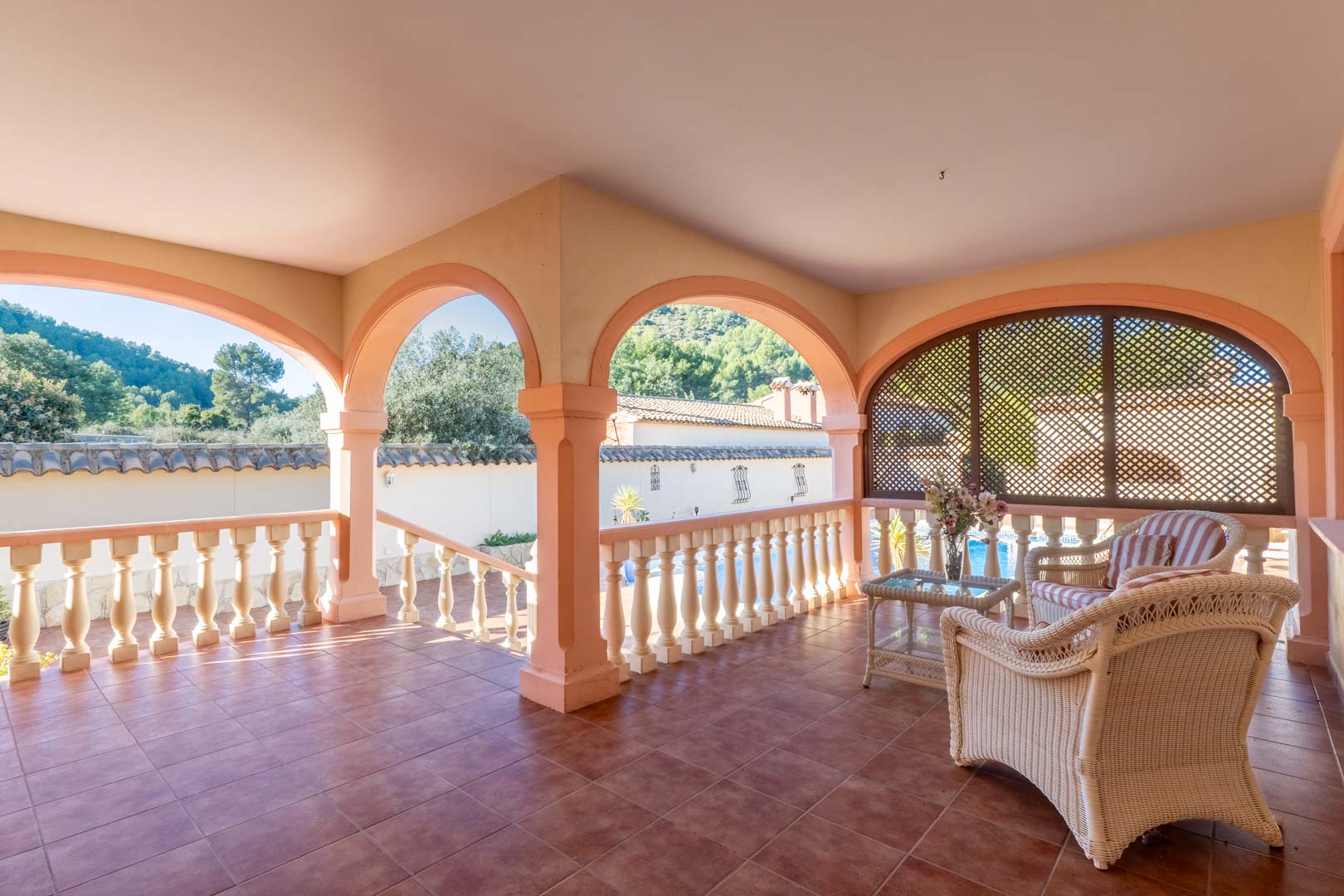 Spacious covered terrace featuring traditional Mediterranean arches, terracotta tiling, and wicker seating with views over the surrounding hills and pool area.