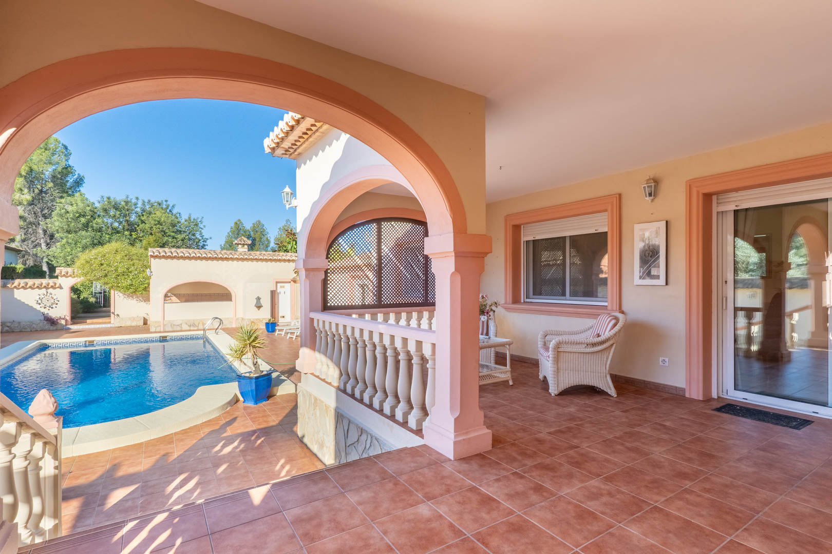 Spacious covered terrace with Mediterranean arches and terracotta flooring, overlooking the private pool area with direct access to the villa's interior.